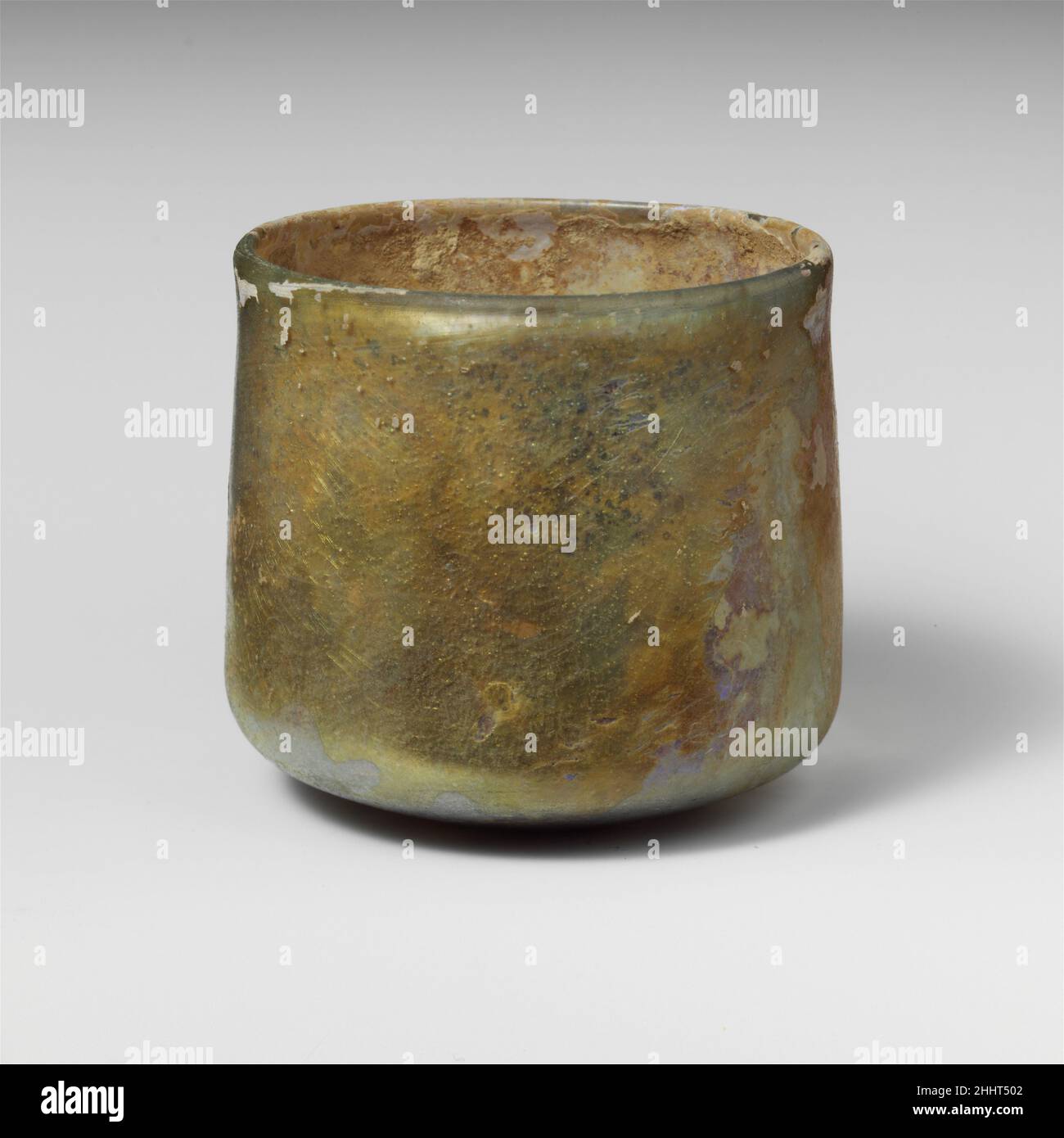 Glasbecher 2nd–3rd century A.D. römisch farblos mit hellblaugrünem Farbton.verdickter, abgerundeter, vertikaler Rand mit leichter Innenlippe; gerader Rand, der sich leicht nach unten ausdehnt, dann in scharfem Winkel nach unten gedreht mit unebenem, konkavem Zentrum.intakt; Nadelstich-Blasen und Blasstreifen; Abstumpfen, Lochfraß und etwas schillernde Verwitterung an der Außenseite; Bodenverkrustungen und cremige Verwitterung im Innenraum. Glasbecher 244613 Stockfoto