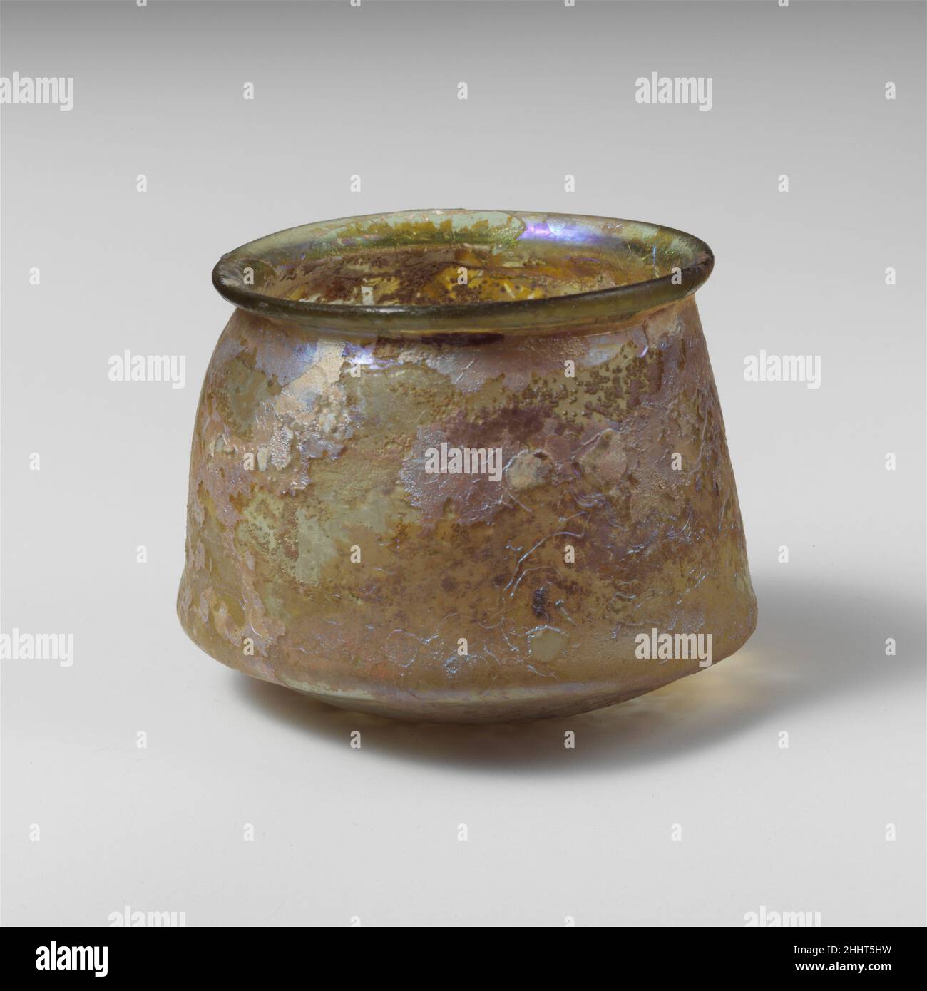 Glasbecher 2nd–3rd century A.D. römisch farblos mit grünlichen Tönungen.Evertierter Rand, mit abgerundeter und verdickter Lippe; ungleichmäßige, wellige Seite, die sich nach unten ausdehnt, mit leicht hervorstehendem Grat an der Basis, dann nach unten gewinkelt mit spitzem tritt in der Mitte.intakt; Nadelstichblasen; Lochfraß und brillant schillernde Verwitterung Etwas Bodenverkrustungen und kalkige Verwitterung im Innenraum. Glasbecher 244612 Stockfoto