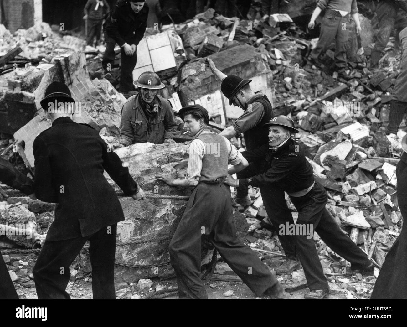 Ein Polizist mit kurzärmeligem Helm versuchte verzweifelt, einen riesigen Felsen im Wrack einer LCC Central School in den Londoner Vororten zu bewegen, nachdem er bei Tageslicht von deutschen Raidern auf dem Dach angegriffen wurde. Mehr als 20 Kinder wurden bei der Razzia getötet. 20th. Januar 1943. Stockfoto