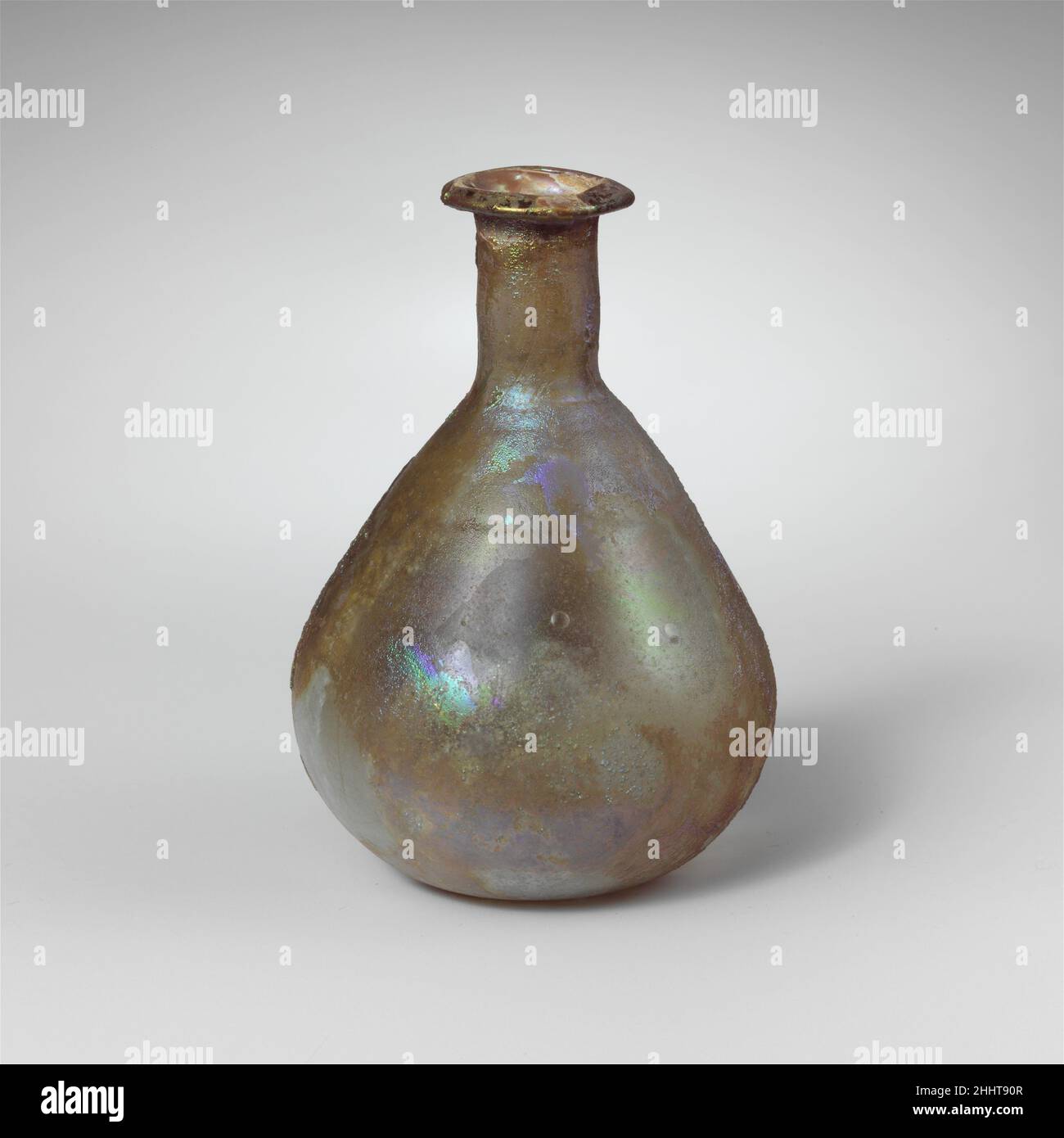 Parfümflasche aus Glas, 1st. Jahrhundert n. Chr., römisch, farblos, mit hellblaugrünem Farbton.Rand ausgeklappt, über und in, mit abgeschrägter Oberfläche; leicht abfackelndem Mund; zylindrischer Hals, leicht um die Basis herum eingedreht; breiter, eiförmiger Körper; kleiner, leicht konkaver Boden.Horizontale, verschraubte Einrückung um den oberen Teil des Körpers.intakt; Nadelstich und ein paar größere Blasen; tiefes Lochfraß und brillant schillernde Verwitterung auf der Außenseite, kalkige Verkrustung und cremig braune Verwitterung auf der Innenseite. Parfümflasche aus Glas 244678 Stockfoto