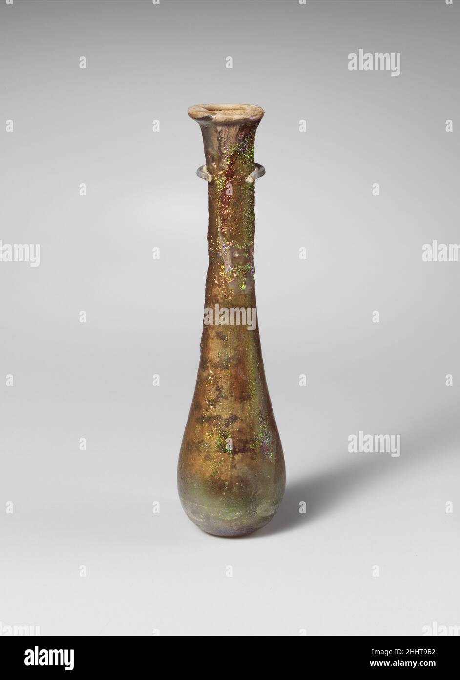 Parfümflasche aus Glas 1st–2nd Jahrhundert n. Chr. römisch farblos mit blassblaugrünem Farbton. Unebener Rand, ausgeklappt, über und in, auf der Oberseite abgeflacht; zylindrischer Hals, nach unten verjüngend, mit tiefem eingedorntem Einrücken um die Basis; länglicher ovoider Körper; kleiner, flacher Boden. Intakt; Nadelblasen und Blasen; Stumpfend, klatschig und brillant schillernde Verwitterung auf der Außenseite, Bodenverkrustungen und cremig-braune Verwitterung auf der Innenseite, mit großen Klumpen Erde innen. Parfümflasche aus Glas 244685 Stockfoto