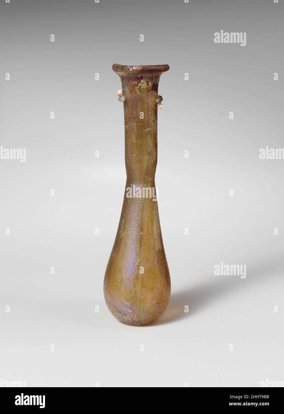 Parfümflasche aus Glas 1st–2nd Jahrhundert n. Chr. römisch farblos mit sehr hellblaugrünen Tönungen und violetten Streifen. Unebener Rand, ausgeklappt, über- und eingefaltet, auf der Oberseite abgeflacht; abfackelter Mund; zylindrischer Hals, leicht nach unten zugeneigt, mit tiefer eingezogenem Einzug um die Basis; länglicher ovoider Körper; Klein, abgeflacht, aber ungleichmäßig bottom.Complete bis auf etwa die Hälfte des Randes und einen Teil des oberen Halses; viele Nadelstichtblasen und Blasstreifen; taumeln, leichtes Lochfraß und brillant schillernde Verwitterung. Parfümflasche aus Glas 244688 Stockfoto