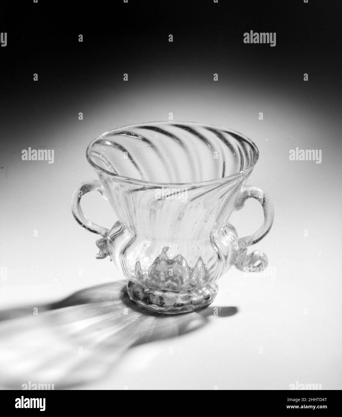 Cup 17th Century Ithury, Venedig (Murano) während der Renaissance wurden venezianische Glasmacher, die auf der Insel Murano arbeiteten, in ganz Europa für ihre feinen und funkelnden Arbeiten gefeiert. „cristallo“ genannt, das die Klarheit des Bergkristalls nachahmt, könnte das Medium in den Händen der erfahrensten Glasbläser wunderbar manipuliert, unterschiedlich gedehnt, papierdünn flach oder spielerisch verdreht oder mit spektakulären Mustern in Formen geblasen werden. Becher. Italienisch, Venedig (Murano). 17th Jahrhundert. Glas. Glas Stockfoto