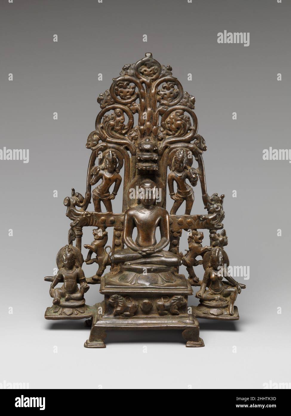 Throned Jina, besucht von einem Yaksha, einem Yakshi und Chauri-Trägern 9th–10th Century India (Karnataka) Diese Digambara-Ikone aus dem Dekkan zeigt eine jina, die unter einem blühenden Baum meditiert, den Konventionen der buddhistischen Skulpturen dieser Zeit folgt. Wie in buddhistischen Bildern wird die jina von Dienern flankiert – die Naturgottheiten Yaksha und yakshi ersetzen die Bodhisattvas – und Fliegenbehahnungsträger, die ihre Bereitschaft zeigen, ihn zu beschenken. Ein Löwe-stützter Thron und dreifache Schirme bestätigen den königlichen Status. In den Pandyan-Gebieten des nördlichen T treten häufig Felsformationen solcher Kompositionen auf Stockfoto