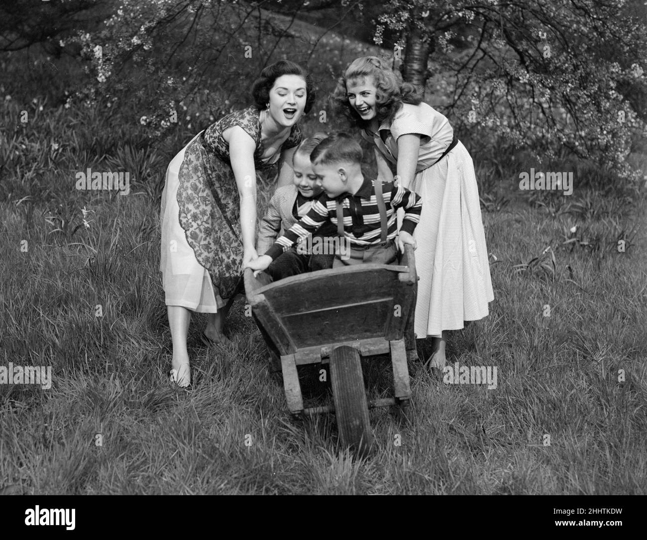 Zwei Mädchen Rollen an einem angenehmen Frühlingstag um 1954 zwei kleine Jungen in einer Schubkarre den Hügel hinunter Stockfoto