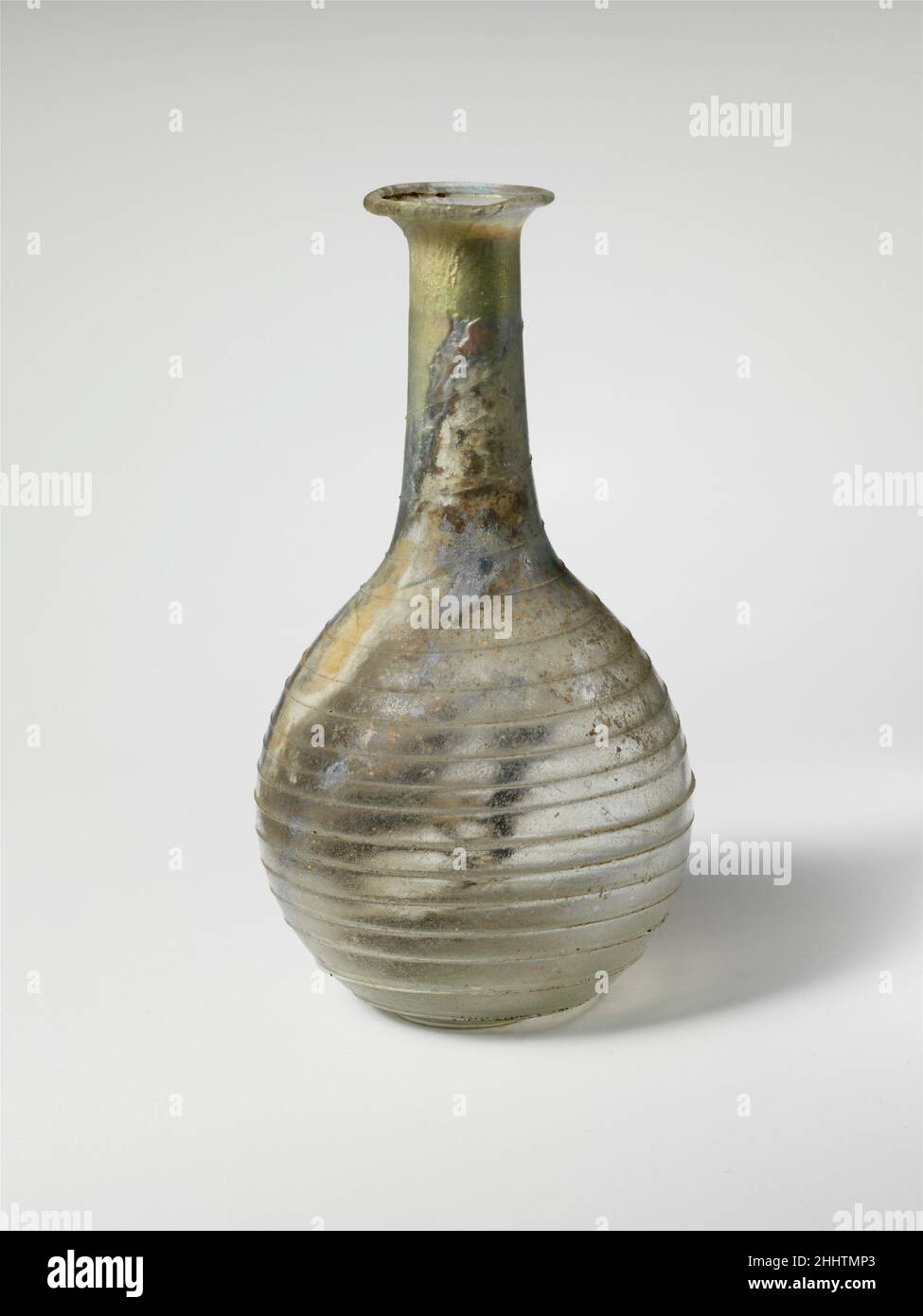 Parfümflasche aus Glas 1st. Jahrhundert n. Chr. römisch farblos, mit Spur in opak-weiß mit grünlichem Farbton. Umgeknickter Rand über und in gefaltet; zylindrischer Hals, sich nach unten ausdehnend; kugelförmiger Körper; Eingeschobene Unterseite.Trail auf den Boden aufgetragen, dann in einer Spirale neunzehn Mal über den Körper gewickelt, endet auf der Oberseite des Halses unter rim.Complete, aber Risse im Körper; Nadelblasen und eine schwarze Verunreinigung in Spur; Stumpfe und schwache Verwitterung auf der Außenseite, Flecken von dicken Böden verkrustert und brillant schillernde Verwitterung auf der Innenseite. Parfümflasche aus Glas 245349 Stockfoto