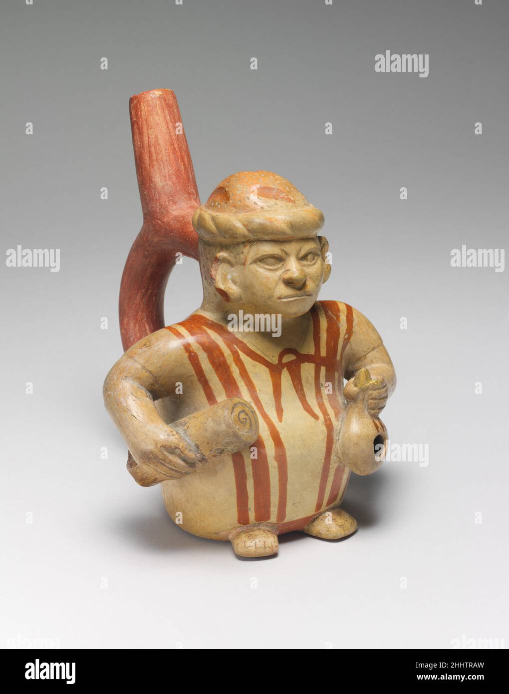 Abbildung Flasche 3rd–5th Century Moche Diese Moche-Flasche mit Steigbügelauslauf stellt einen Mann dar, der eine ärmlige Tunika mit vertikalen Bändern trägt und Grabbeigabeartikel trägt. Er hält eine gerollte Matte in seiner rechten Hand und einen Dipper in seiner linken Hand. Ähnliche Moche-Gefäße stellen verstümmelte Individuen, Skelettwesen und anthropomorphe Fledermäuse dar, die die gleiche Aktion ausführen. Die Vorbereitung der Körper, ihrer Umhüllungen, Einhüllungen und Grabbeigaben war ein aufwändiger Prozess in der Moche-Gesellschaft. Der Körper wurde zuerst in eine oder mehrere Schichten von Textilien eingewickelt, dann in eine Rohrstruktur oder in eine Fasermatte, a, eingehüllt Stockfoto