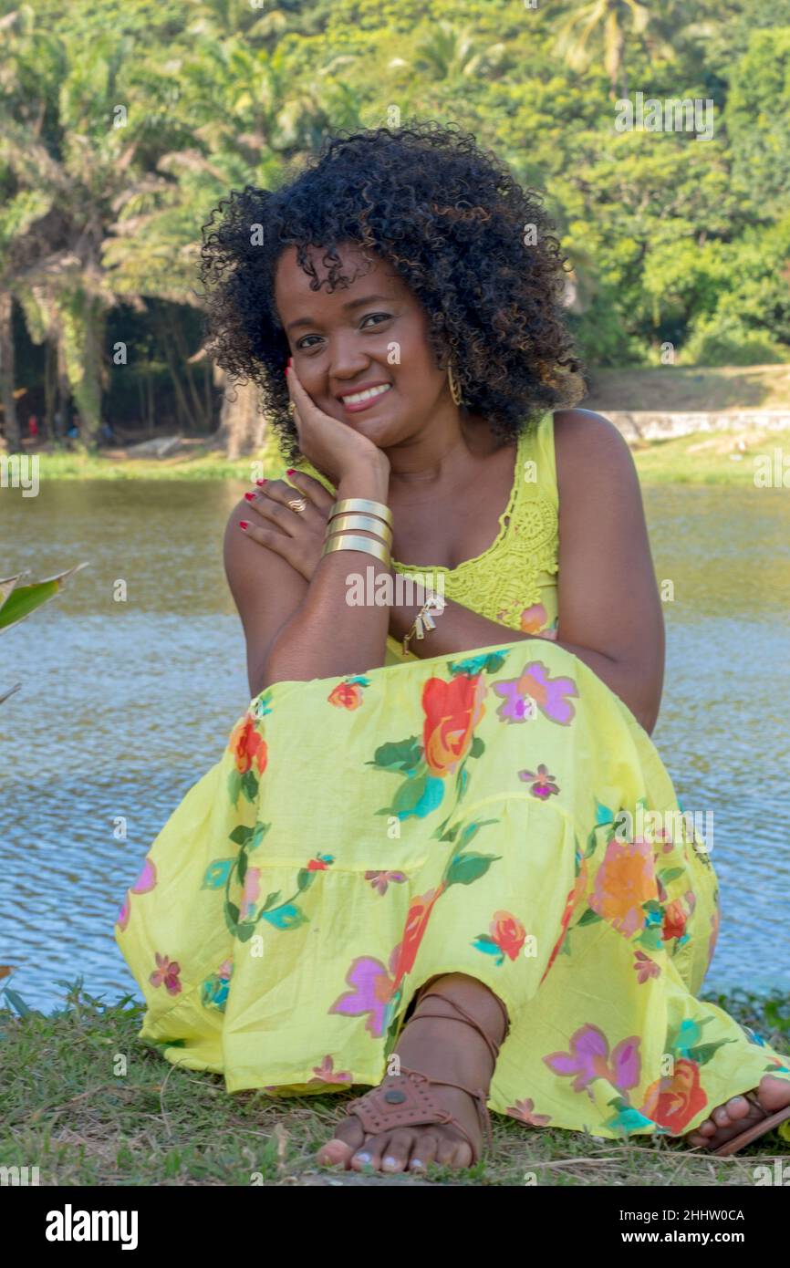 Schwarze Frau posiert für Foto. Sie trägt Gelb, lächelt und schaut auf die Kamera. Salvador, Bahia, Brasilien. Stockfoto