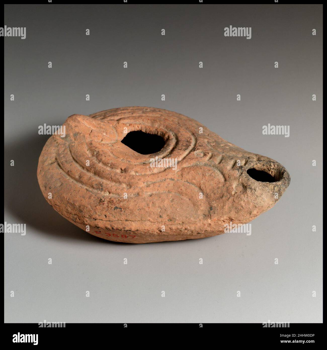 Terrakotta-Öllampe 3rd Jahrhundert A.D. Roman Vessberg Typ 19. Formgefertigte, konische Griffform. Scharf karierter Körper; zentrales Einfüllloch, umgeben von einem erhöhten Kreis; auf der Schulter Muster aus parallelen, eingeschnittenen Rillen um die Seiten und den Rücken sowie ein Muster aus eingeprägten Punkten und kurzen Linien hinter dem Dochtloch mit erhöhtem Rand; Kanal zu Dochtloch. Flacher Boden mit zwei konzentrischen Nuten und einem zentralen Punkt.intakt. Das Dochtloch wurde im mittleren, schlichten Diskus grob gebildet. Terrakotta-Öllampe. Roman. 3rd Jahrhundert n. Chr.. Terrakotta. Spätkaiserlich. Terrakotta Stockfoto