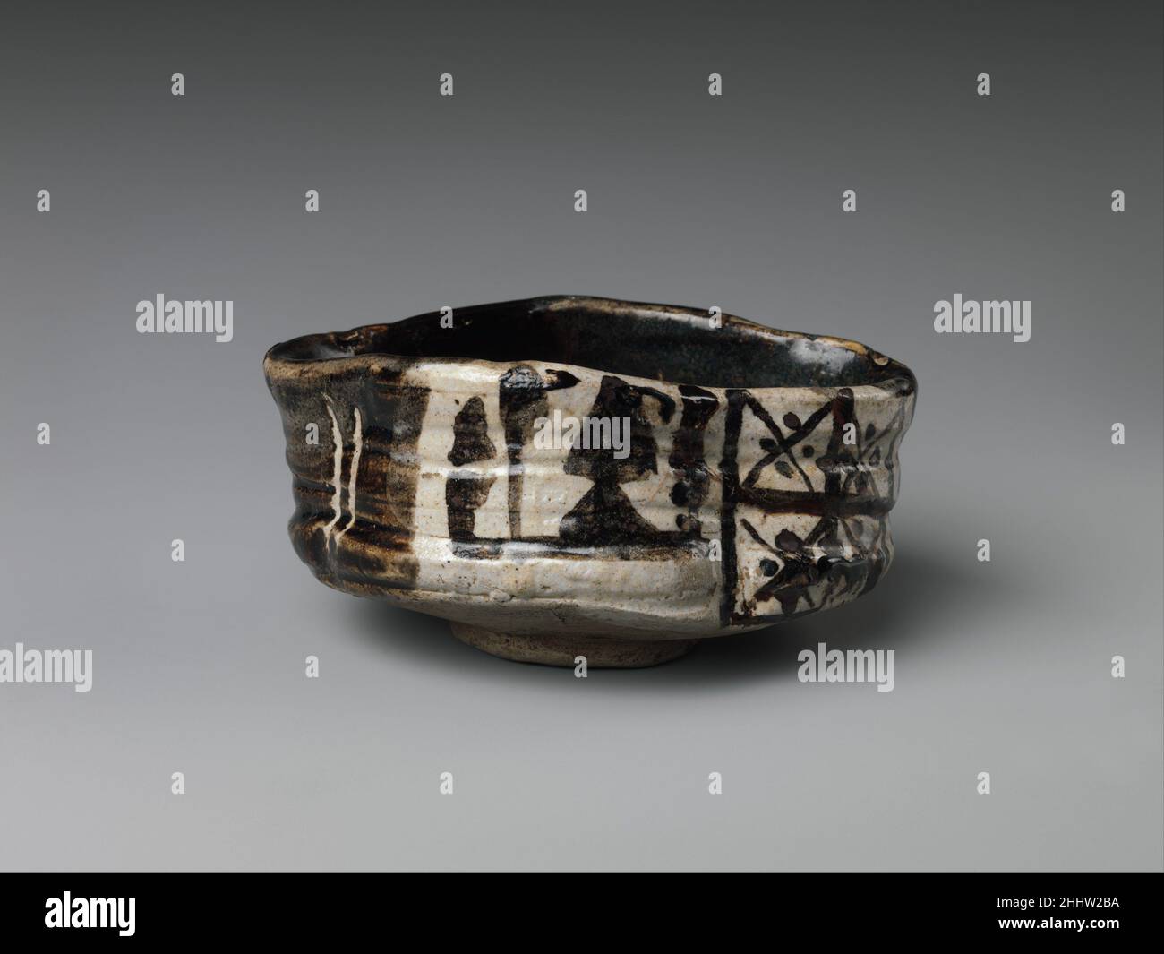 Clog-förmige Teeschale (Chawan) mit Pflaumenblüten und geometrischen Mustern Anfang des 17th. Jahrhunderts Japan Teeschalen im Oribe-Stil wurden oft so etwas wie alte Clogs geformt und als Kutsugata oder "Clog-förmige" beschrieben. Nachdem sich eine runde Teeschale auf dem Rad gebildet hatte, wurde sie an mehreren Stellen eingerückt, wodurch die kreisförmige Form zerstört und eine asymmetrische Form entstand. Die Außenfläche der Schüssel wurde dann mit einem Teigschaber bearbeitet, um sie rau und uneben zu machen. Extravagante Verzerrungen und Unregelmäßigkeiten dieser Art charakterisieren die Ästhetik der Oribe Ware.Diese Teeschale ist lebenswichtig, organisch-seemin Stockfoto