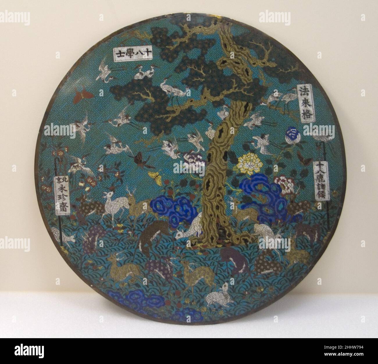 Scheibe mit verheißungsvollen Bildern Ende des 19.–Anfang des 20th. Jahrhunderts China Hirsche und Kraniche sind allgegenwärtige chinesische Motive, die für gute Wünsche stehen, ebenso wie die Kiefer in der Mitte dieser Tafel. Ähnliche Themen werden in zwei der Inschriften wiederholt. Die Inschrift auf einem Banner links unten ist der Name eines Antiquitätenladens, der in Peking Ende des 19. Und Anfang des 20. Jahrhunderts aktiv war; Das oben rechts zeigt den chinesischen Namen von E. Farago, einem Beamten des Zolls, der am Hof des Guangxu-Imperators (r. 1871–1908). Disc mit „Aussicious Images“ 40742 Stockfoto