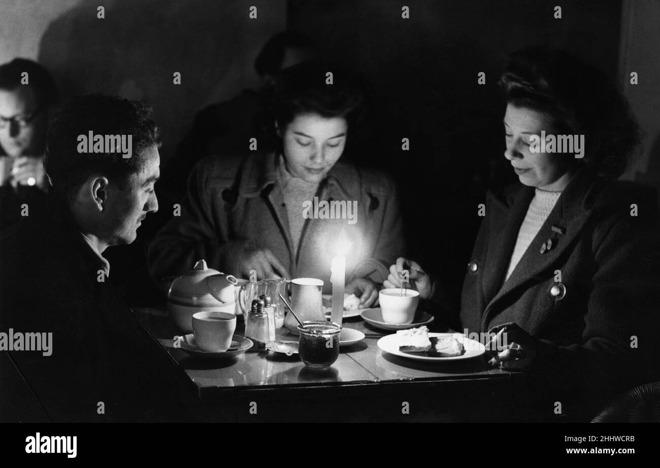 Im Winter 1946 - 1947 erlebte das Vereinigte Königreich mehrere Kältewellen, die am 21. Januar 1947 begannen und große Schneeverwehungen ins Land brachten, die Straßen und Eisenbahnen blockierten. Die Kohlelieferungen, die nach dem Zweiten Weltkrieg bereits niedrig waren, kämpften um die Versorgung mit Kraftwerken, und viele Kraftwerke mussten aufgrund des Mangels an Treibstoff stillgelegt oder auf einem niedrigeren Niveau produzieren. Die Regierung von Attlee führte mehrere Maßnahmen zur Senkung des Stromverbrauchs ein, darunter die Beschränkung des häuslichen Stroms auf 19 Stunden pro Tag und die Reduzierung der industriellen Versorgung.Unser Bild zeigt: Tee bei Kerzenlicht in einer Stadt von Lo Stockfoto