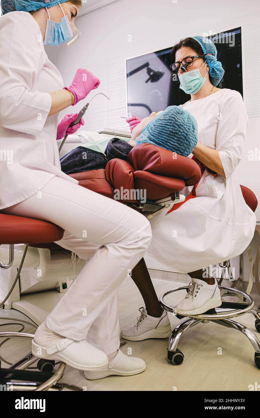 Zahnärzte arbeiten in der modernen Stomatologie Klinik zusammen mit einem Assistenten mit stomatologischen Instrumenten machen Zähne Heilung Verfahren für einen Patienten Stockfoto