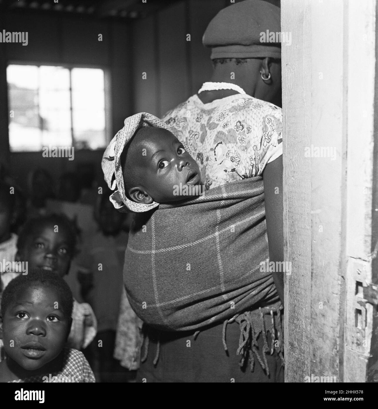 Mutter, die ihr Baby in einem Papoose trägt, besucht eine lokale Gesundheitsklinik im Township Langa in der Nähe von Kapstadt. 4th. Februar 1955 Stockfoto