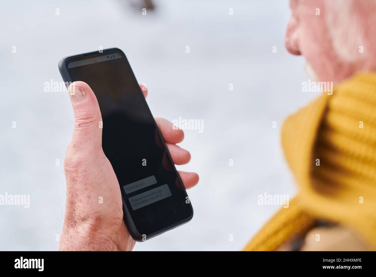 Hand eines älteren Mannes in gelbem Strickschal, der das Smartphone hält, während er am Wintertag im Freien eine neue Botschaft liest Stockfoto