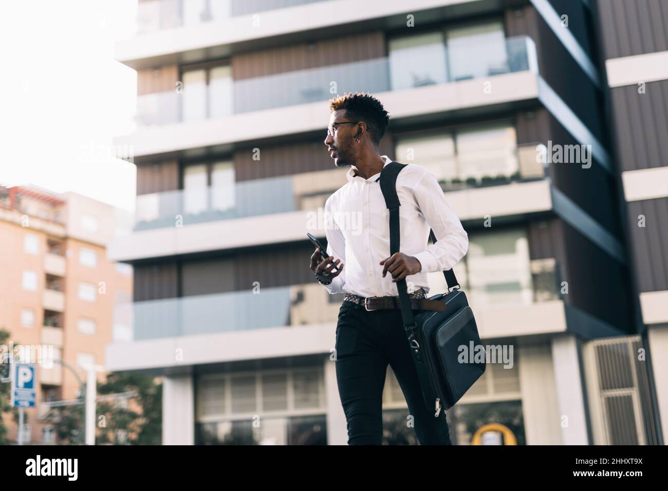 Der junge afroamerikanische Geschäftsmann überquert in Eile mit einem Smartphone in der Hand eine Straße Stockfoto