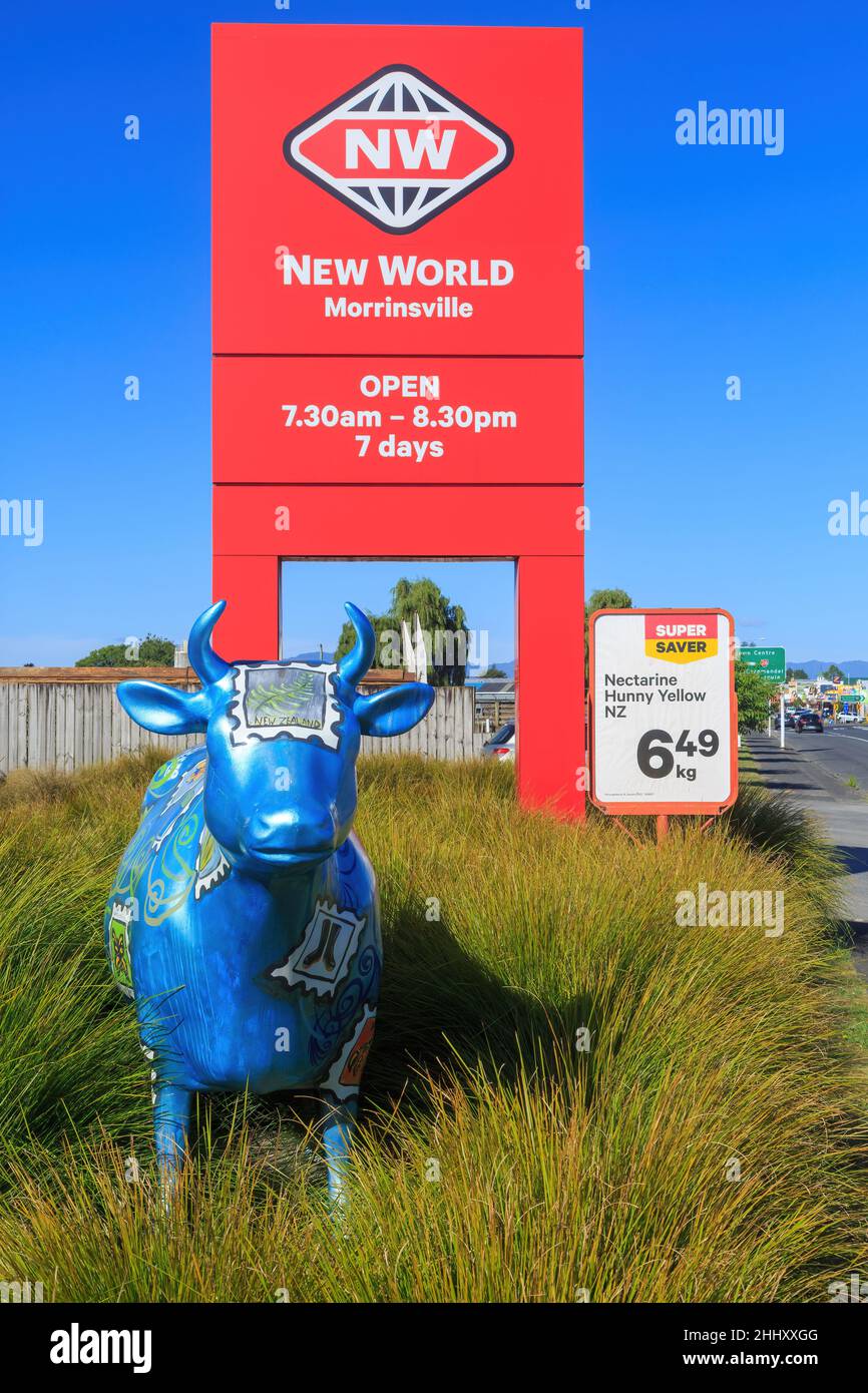 Eine Skulptur einer Kuh und ein New World Supermarkt Schild in Morrinsville, Neuseeland. Die vielen Kuhskulpturen der Stadt sind eine Touristenattraktion Stockfoto