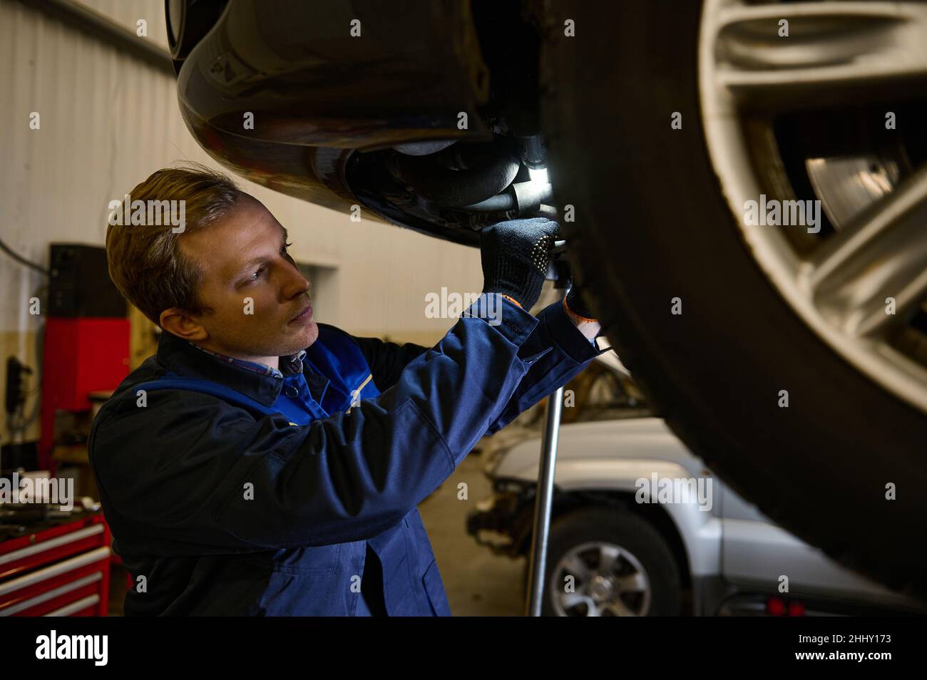 Mechaniker, der die Ausrichtung des Fahrzeugs überprüft, indem er das Chassis mit einer Lampe überprüft. Der Autoingenieur überprüft den Reifen im Wartungscenter. Techniker oder Engi Stockfoto