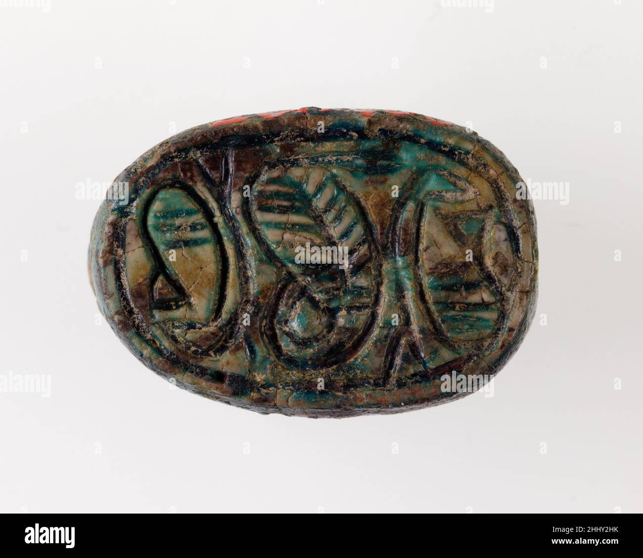 Skarabäus mit Uraeus- und Papyrus-Pflanzen ca. 1740–1640 v. Chr. Reich der Mitte Ein großer Uraeus, dessen Schwanz sich hinter ihm zusammengerollt hat und dessen Körper mit feinen geschlüpften Linien verziert ist, dominiert das Design auf der Unterseite dieses Skarabäus aus dem späten Reich der Mitte (späte Dynastie 12–13, ca. 1850-1640 V. CHR.). Auf beiden Seiten befinden sich Papyrus-Pflanzen, die aus einem geraden und einem gebogenen Stamm bestehen. Sie werden tête-bêche, also auf dem Kopf zueinander, platziert, und parallele Linien verbinden die Stämme. Pflanzen sind ein beliebtes Thema auf ägyptischen Robbenamulette, weil sie sich auf Leben, Erneuerung und Regeneration beziehen, und während des Mittleren Reiches Stockfoto