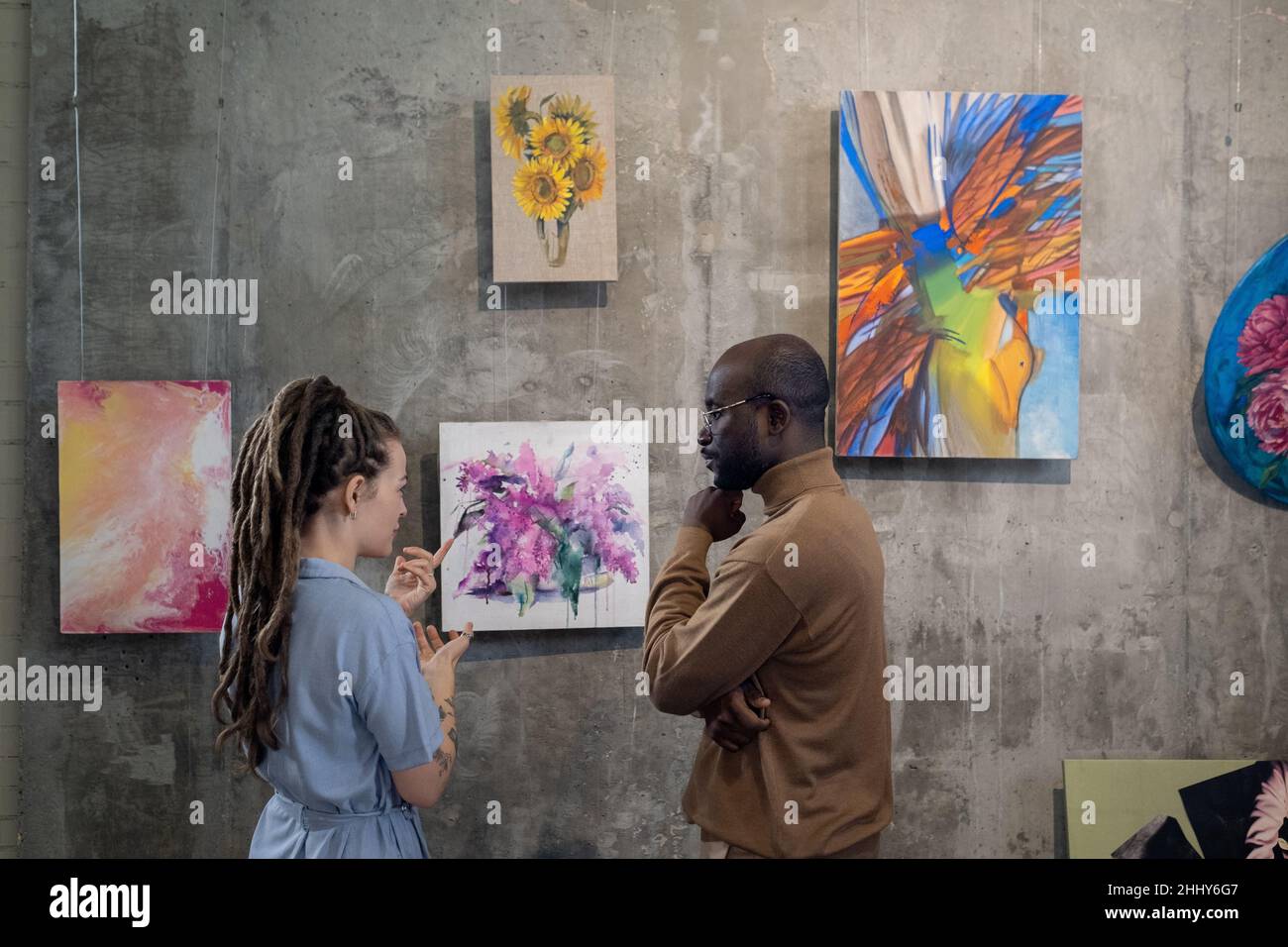 Junge Frau diskutiert mit afrikanischem Mann Bilder an der Wand, während sie in der Kunstgalerie stehen Stockfoto