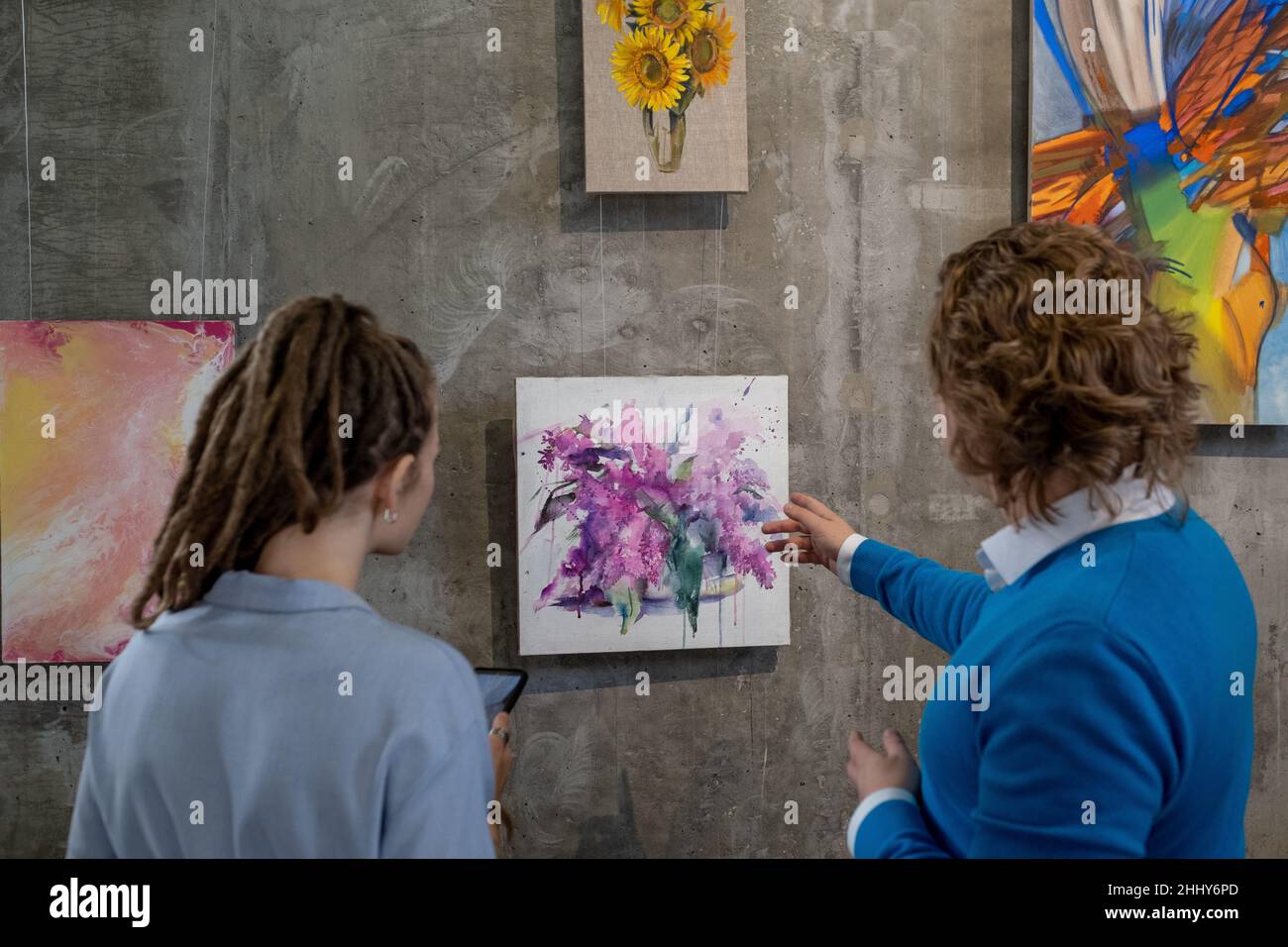 Rückansicht des Kunstführers, der während der Ausstellung auf die Malerei zeigt und mit der jungen Frau spricht Stockfoto