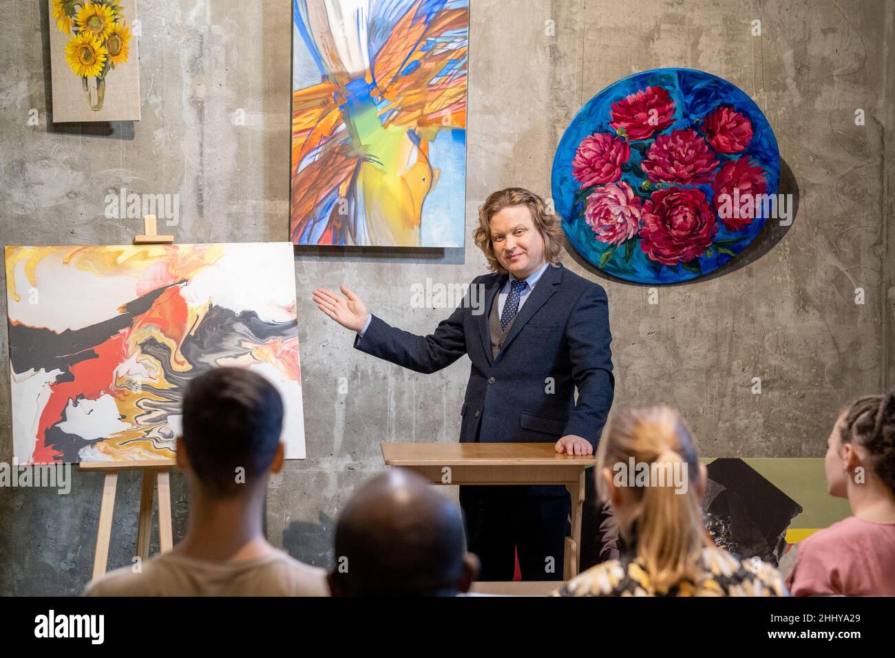 Reifer Maler im Anzug, der während seiner Präsentation in der Kunstgalerie seine Bilder den Menschen präsentiert Stockfoto