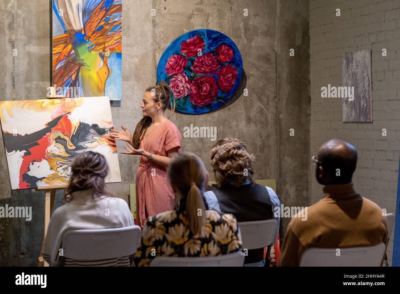 Junge Frau zeigt auf Malerei und präsentiert die moderne Kunst für die Menschen während der Präsentation in der Kunstgalerie Stockfoto