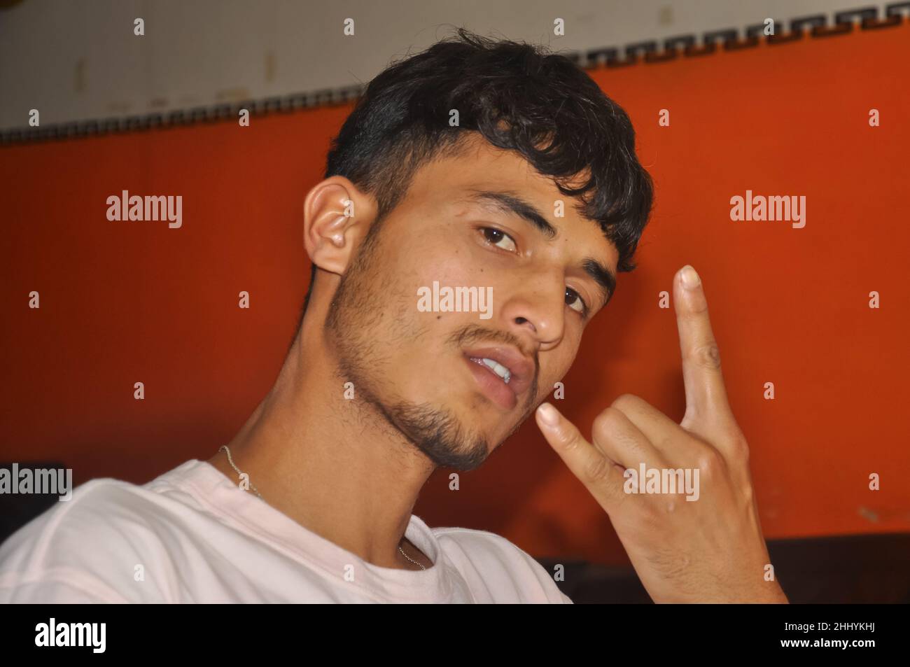 Nahaufnahme eines jungen südasiatischen Mannes, der mit seiner Hand eine Rock-Hand-Geste zeigt, drinnen sitzend, mit Blick auf die Kamera Stockfoto
