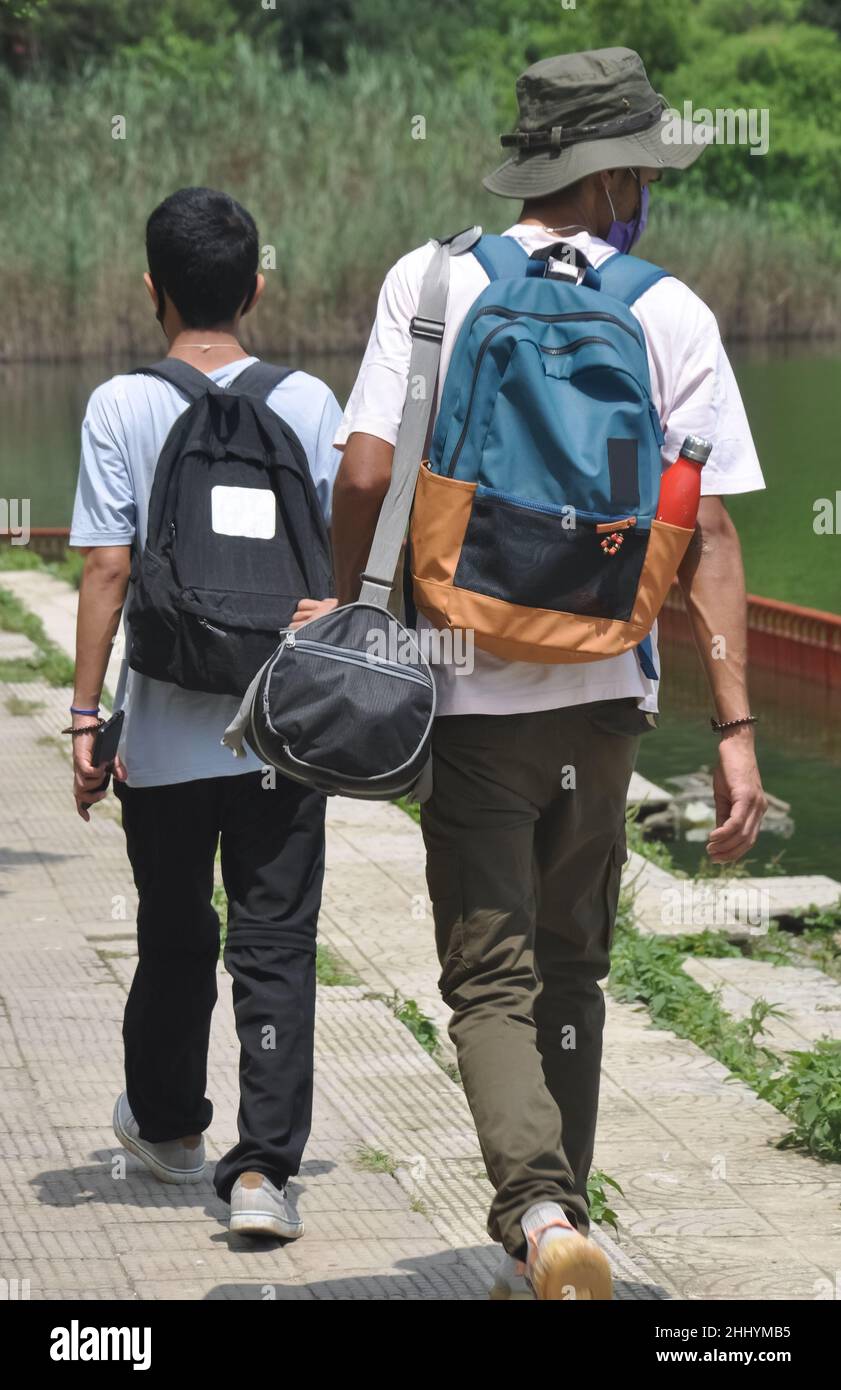 Rückansicht von zwei männlichen Touristen, die Gesichtsmaske mit Rucksack  tragen und am See spazieren gehen. Reisen während einer  Coronavirus-Pandemie Stockfotografie - Alamy