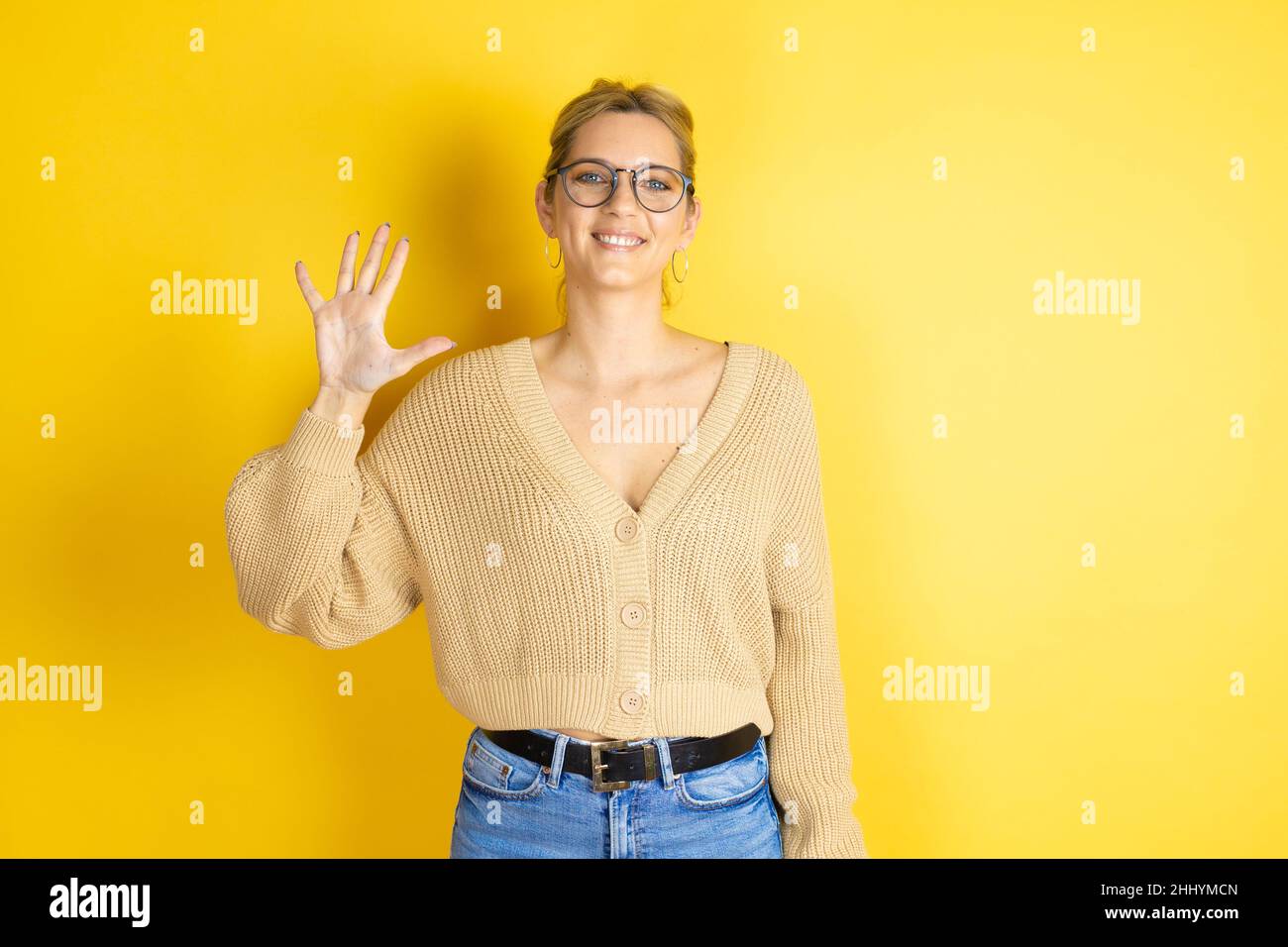 Junge schöne Frau trägt lässigen Pullover über isolierten gelben Hintergrund zeigt und zeigt mit den Fingern Nummer fünf, während sie zuversichtlich lächelt Stockfoto