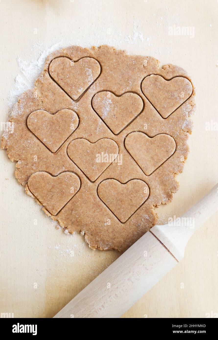 Der Prozess der Herstellung von herzförmigen Vollkornmehl-Cookies. Das Konzept des festlichen Hausbackens. Valentinstag. Draufsicht. Vertikale Ausrichtung. Stockfoto