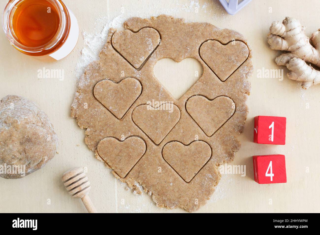 Der Teig wird mit einem Herz-Ausstecher mit Zutaten rund und Holzwürfeln mit der Nummer 14 ausgeschnitten. Festliches Backkonzept für valentine's da Stockfoto