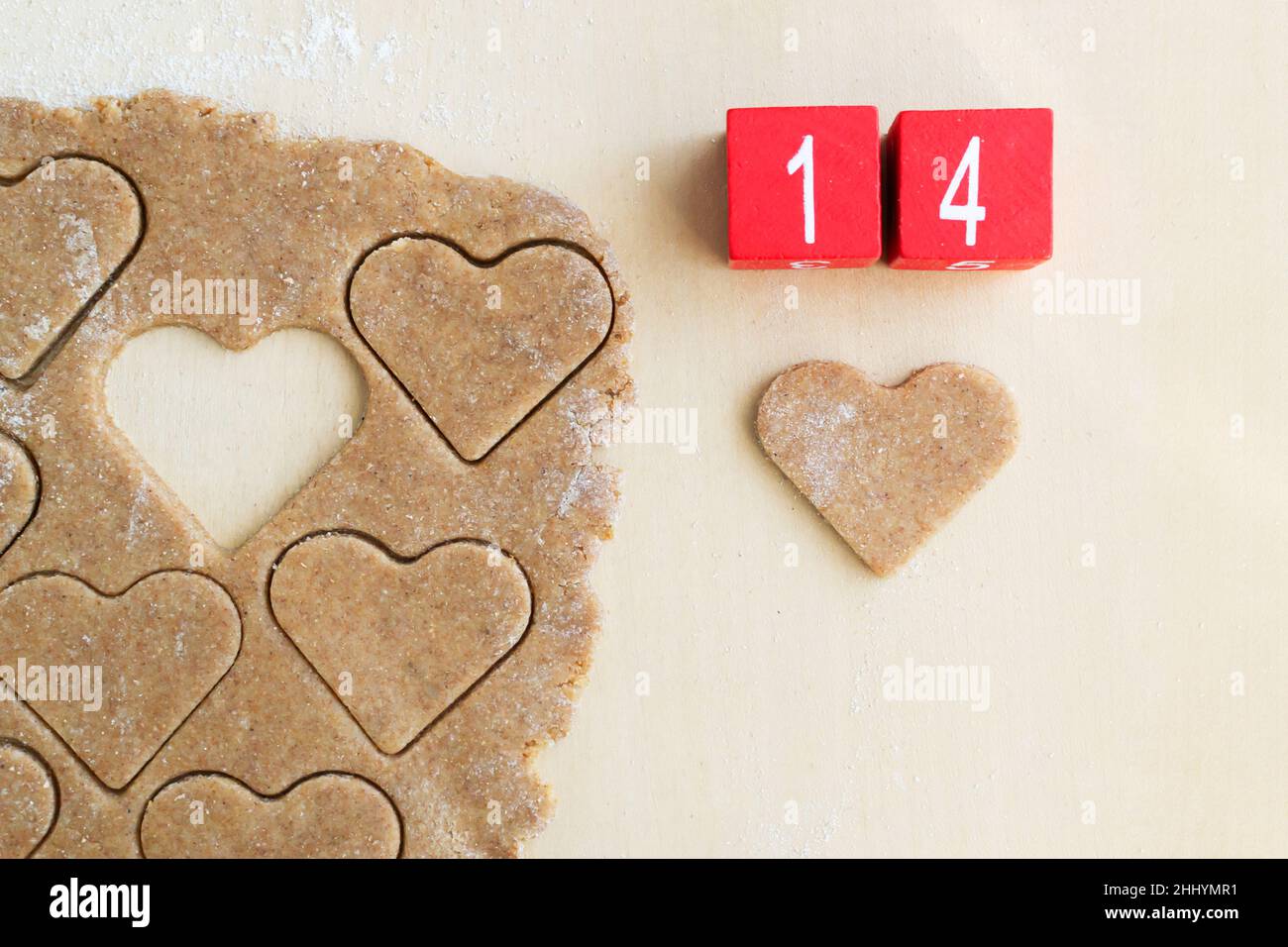 Der Teig wird in Form eines Herzens und Holzwürfeln mit der Zahl 14 geschnitten. Das Konzept des Feiertagsbackens zum Valentinstag. Draufsicht. Stockfoto