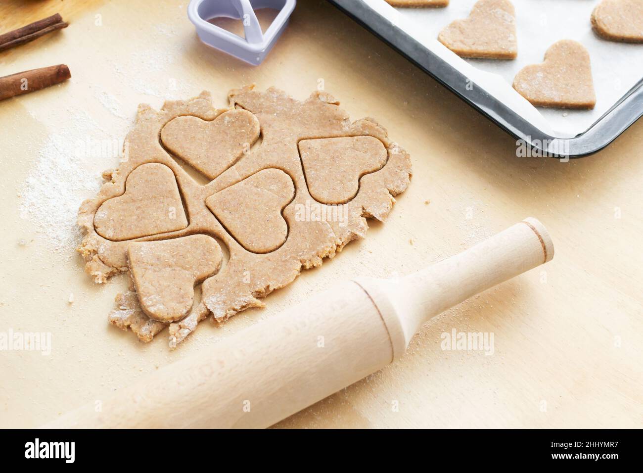 Cookies schneiden in Form eines Herzens mit einem Nudelholz auf einem hölzernen Hintergrund aus. Der Prozess der Herstellung von Urlaubsklätzchen zum Valentinstag. Home Bak Stockfoto