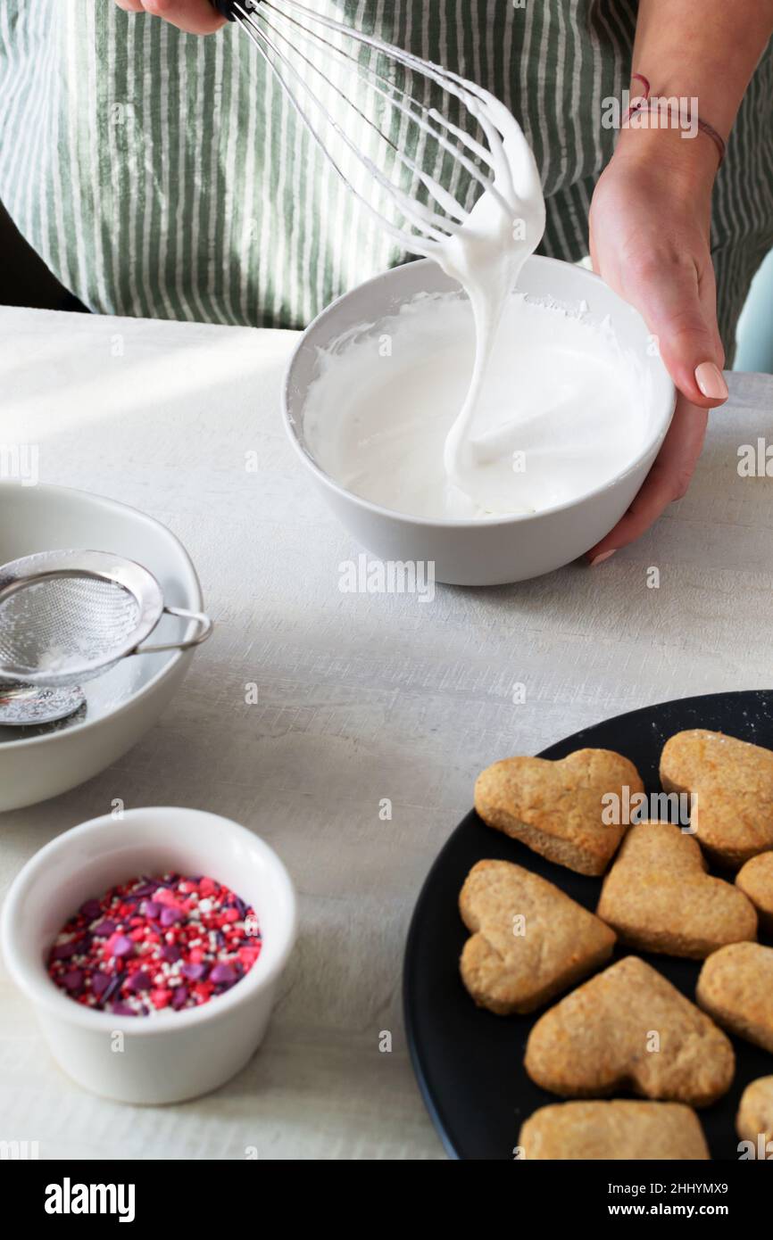Erstellung von Vereisung. Fertige Kekse müssen dekoriert werden. Der Prozess der Herstellung von Urlaubsklätzchen zum Valentinstag. Mit Liebe zu Hause backen. Vertikal o Stockfoto
