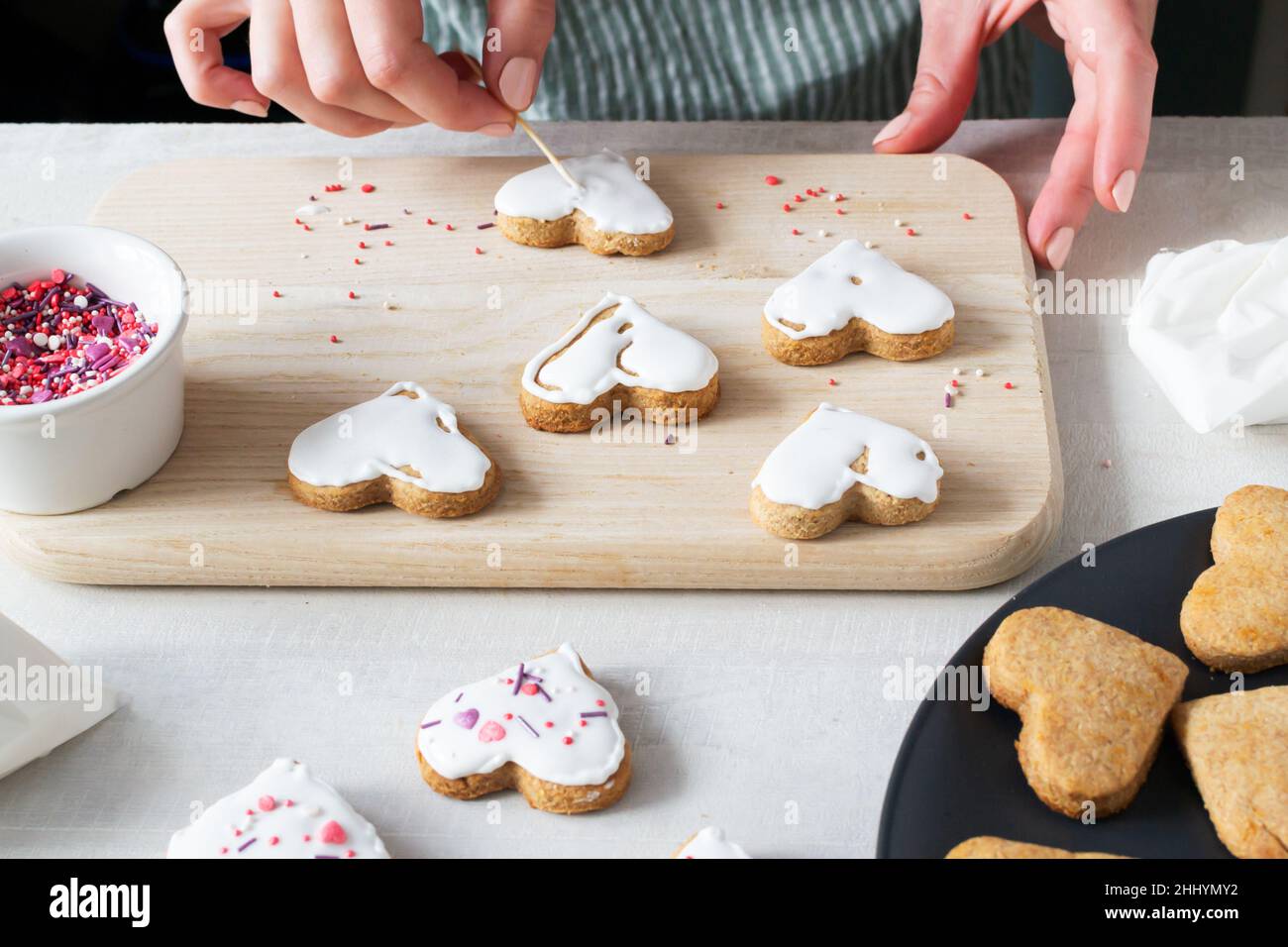 Damenhände schmücken Ready Cookies mit Glasur. Der Prozess der Herstellung von Urlaubsklätzchen zum Valentinstag. Mit Liebe zu Hause backen. Horizontale Orientat Stockfoto