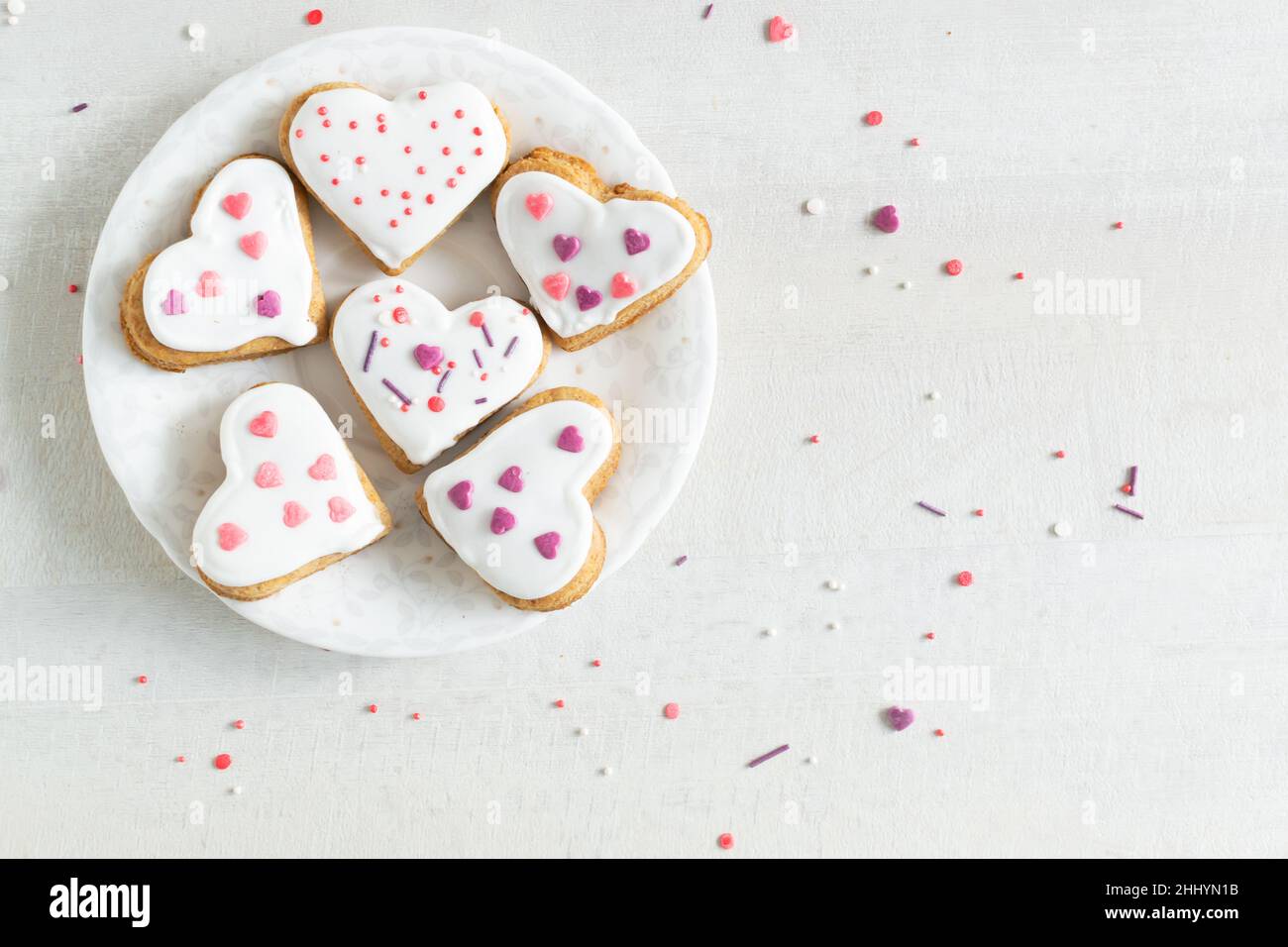 Lebkuchen mit weißer Glasur bedeckt und auf einer hellen Untertasse auf einem hellen Hintergrund bestreuen. Das Konzept des Backens zum Valentinstag. Ansicht von oben. Kopieren Stockfoto