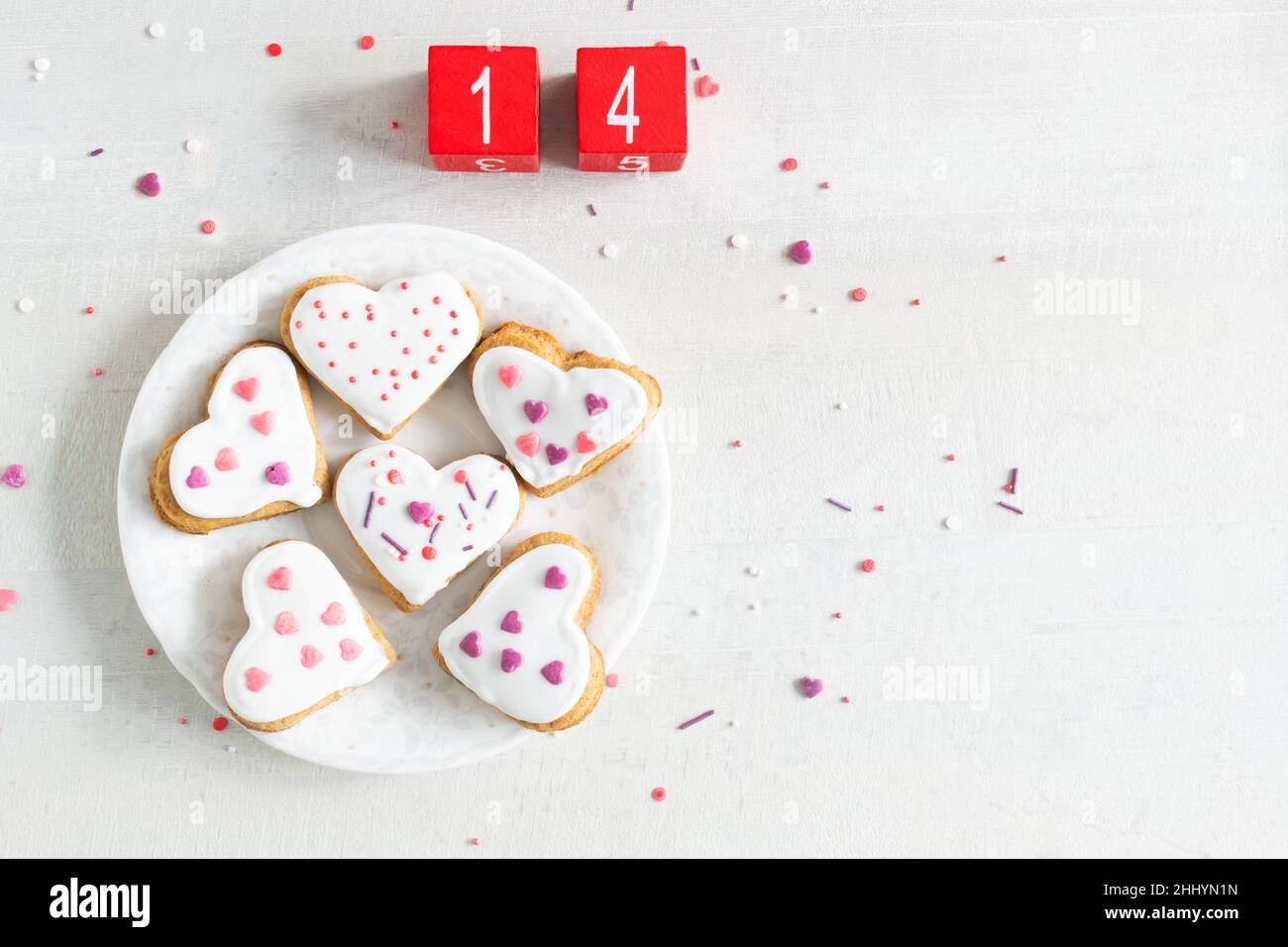 Lebkuchen mit weißer Glasur bedeckt und auf einer leichten Untertasse mit roten Würfeln mit den Zahlen 14 bestreuen. Das Konzept des Backens zum Valentinstag. T Stockfoto