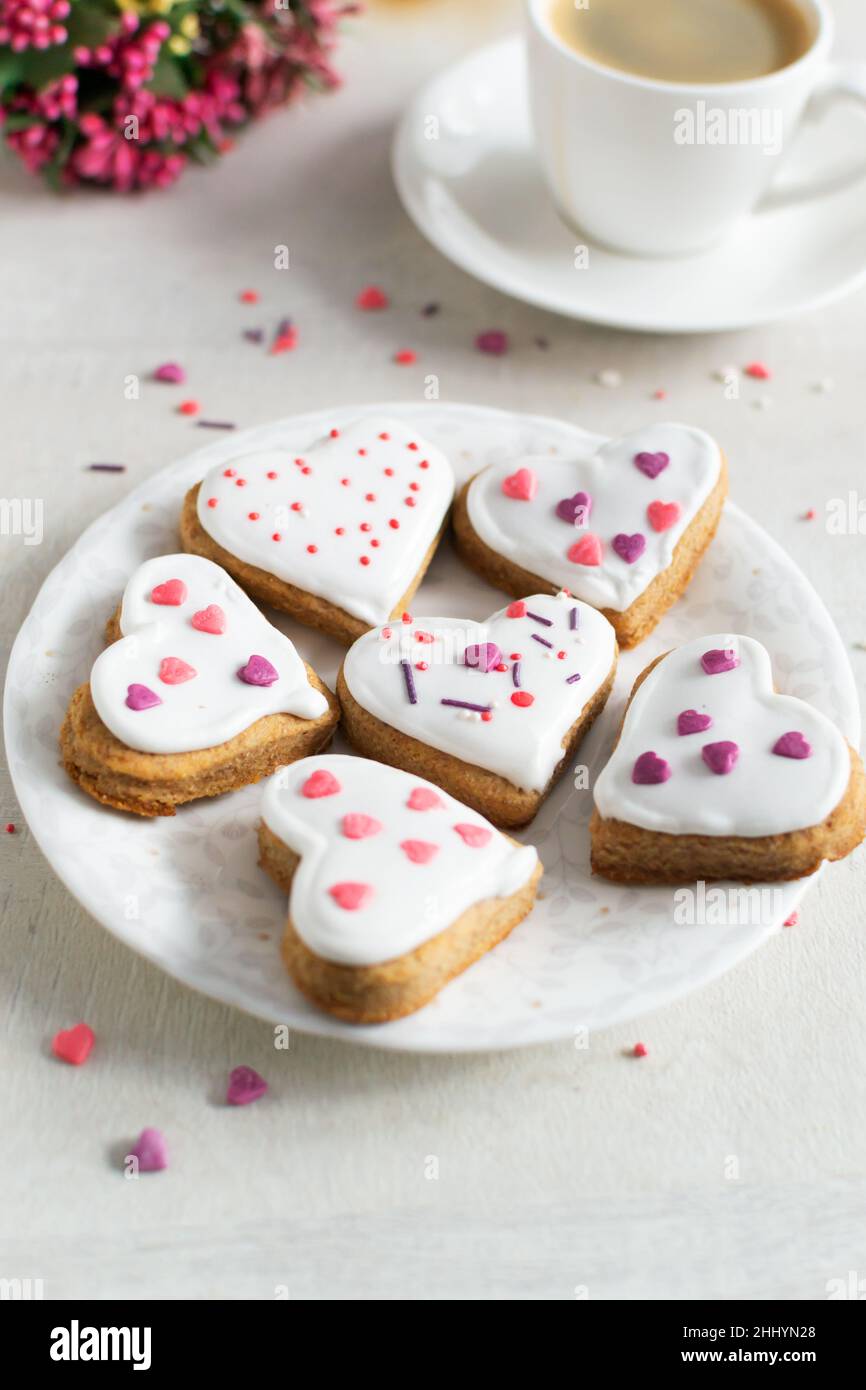 Lebkuchen mit weißer Glasur bedeckt und auf einer hellen Untertasse mit einer Tasse Espresso und Blumen im Hintergrund bestreuen. Das Konzept des Feierns Stockfoto