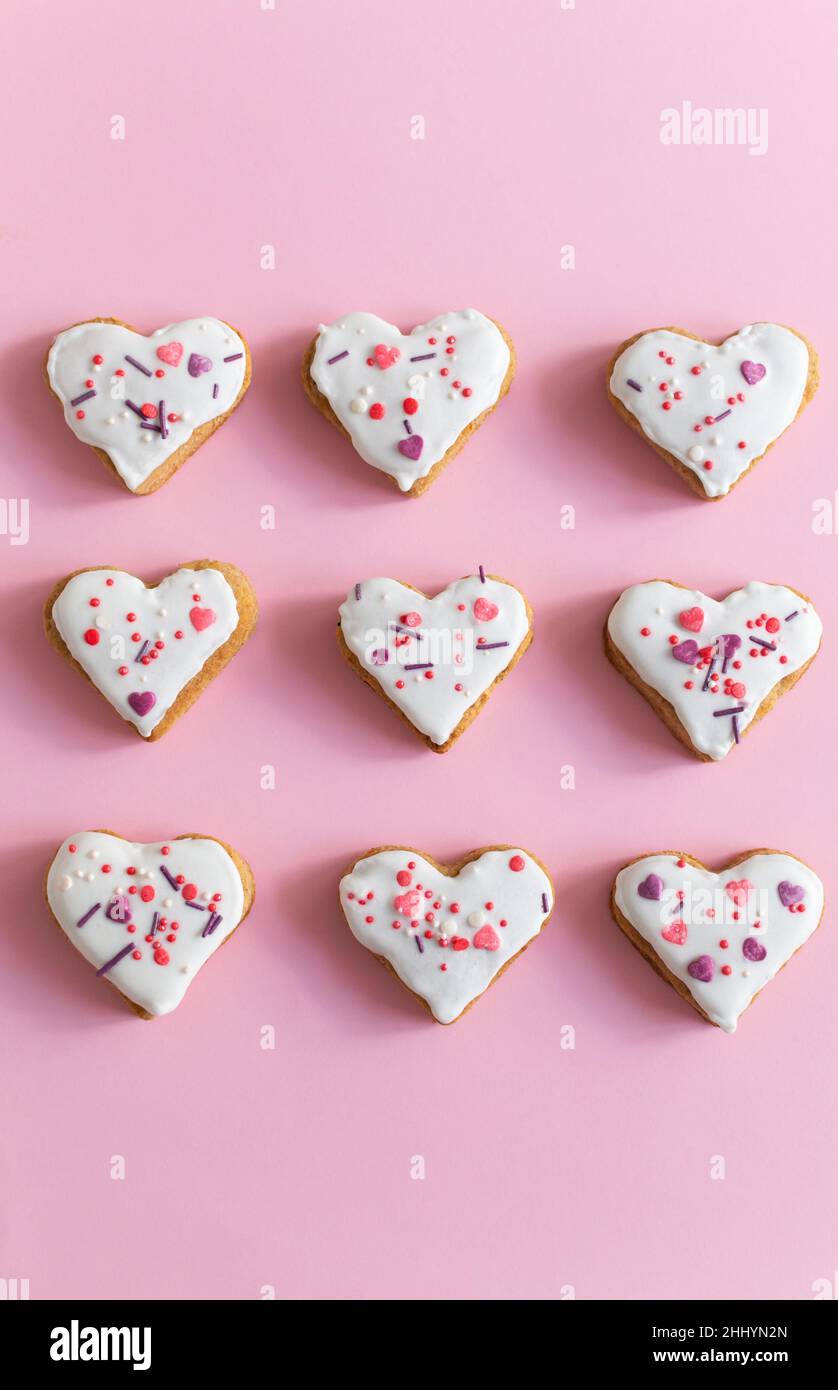 Lebkuchen mit weißer Glasur bedeckt und auf einem rosa Hintergrund bestreut. Das Konzept der Feier des Valentinstag. Vertikale Ausrichtung. Draufsicht. Stockfoto