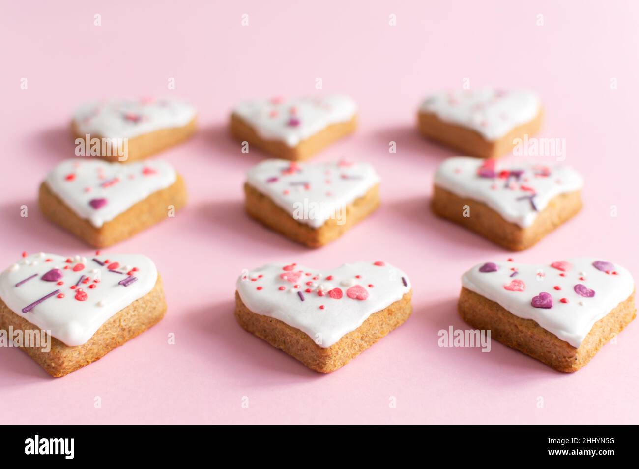 Lebkuchen mit weißer Glasur bedeckt und auf einem rosa Hintergrund bestreut. Das Konzept der Feier des Valentinstag. Horizontale Ausrichtung. Selektiv Stockfoto