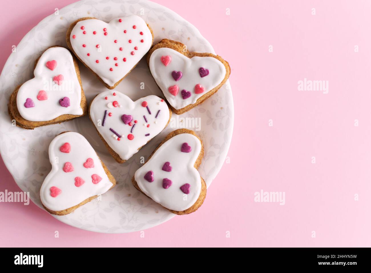 Lebkuchen mit weißer Glasur bedeckt und auf einer weißen Untertasse auf einem rosa Hintergrund bestreut. Das Konzept der Feier des Valentinstag. Horizontale oris Stockfoto