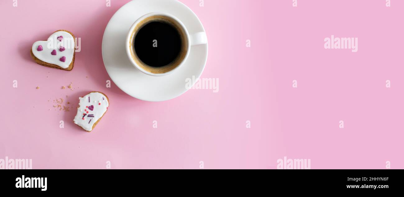 Weiße Tasse und Untertasse mit Espresso und Lebkuchen mit weißer Glasur bedeckt und bestreuen auf einem rosa Hintergrund. Das Konzept der Feier zum Valentinstag Stockfoto