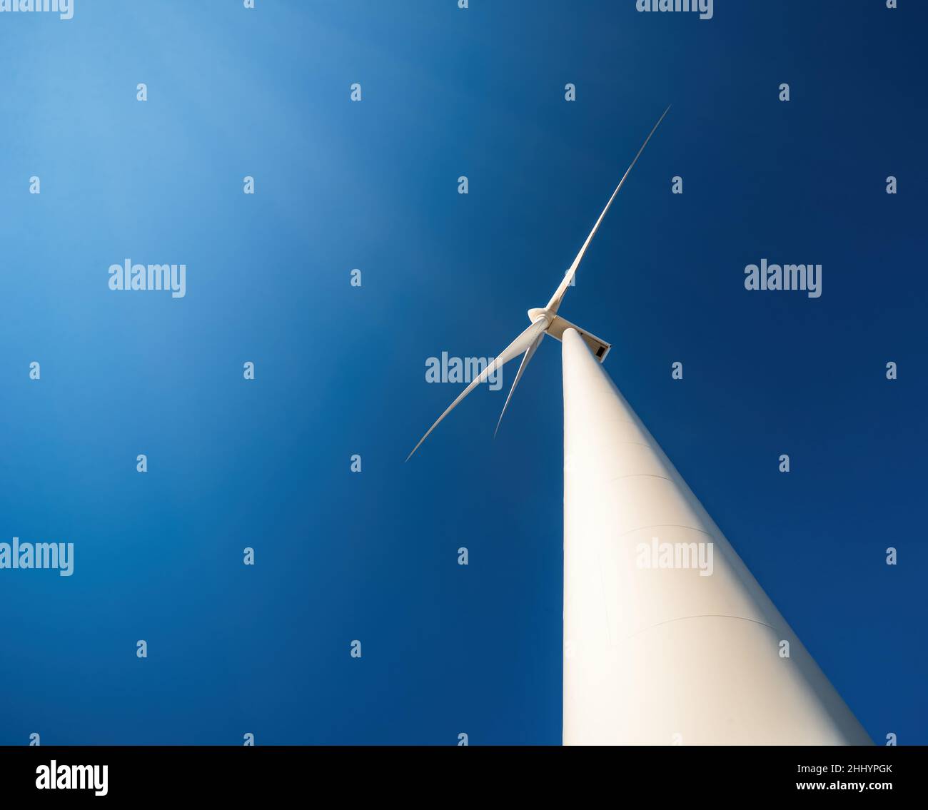 Windgenerator gegen blauen Himmel. Minimalistische Aufnahme, niedriger Blickwinkel, dramatische Perspektive Stockfoto