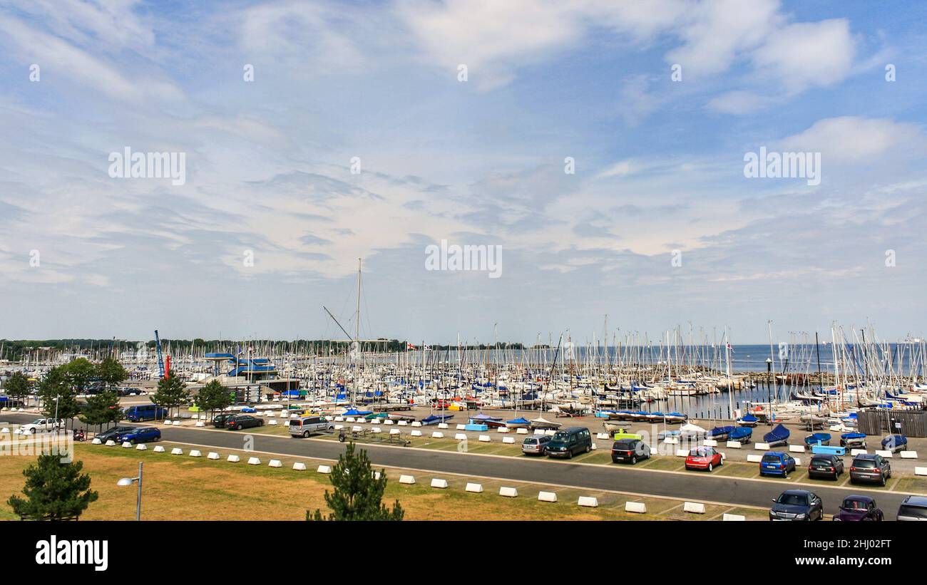 Blick auf Segelboote, die am Pier angedockt sind, und Parkplätze, die im Sommer vom Segelzentrum der Universität Kiel aus mit Wolken im blauen Himmel im Hintergrund betrachtet werden. Stockfoto
