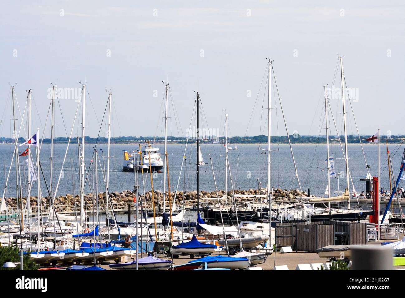 Segelboote dockten an der Pier an, mit einem Schlepper im Hintergrund, der im Sommer vom Segelzentrum der Universität Kiel aus gesehen wurde. Blauer Himmel. Stockfoto
