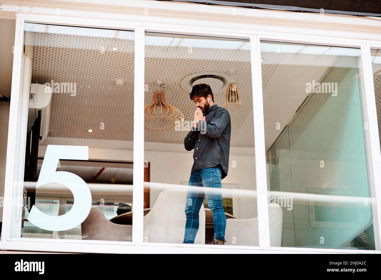 Ich hoffe, das klappt. Aufnahme eines jungen Geschäftsmannes, der ängstlich aussieht, während er an einer Glaswand in einem Büro steht. Stockfoto