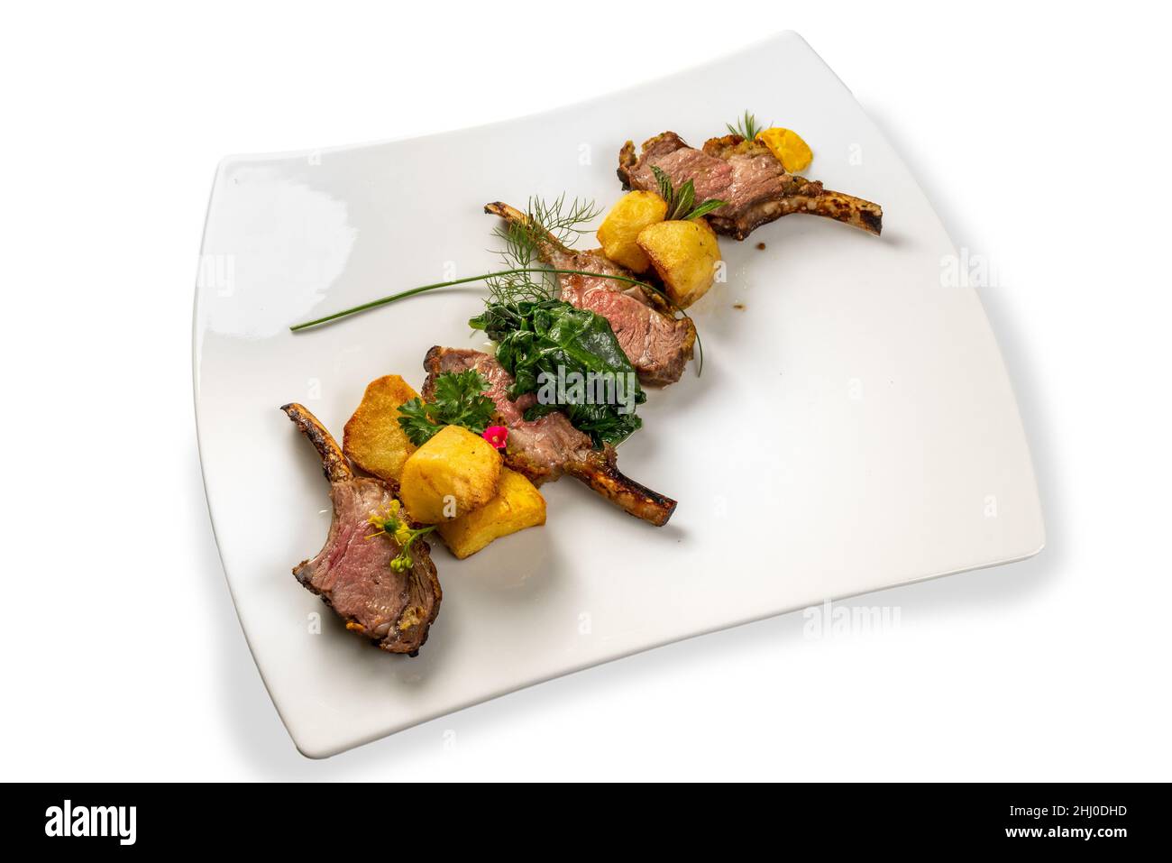 Geröstete Lammkoteletts mit Kartoffeln, Spinat und Kräutern auf weißem Teller isoliert auf Weiß Stockfoto