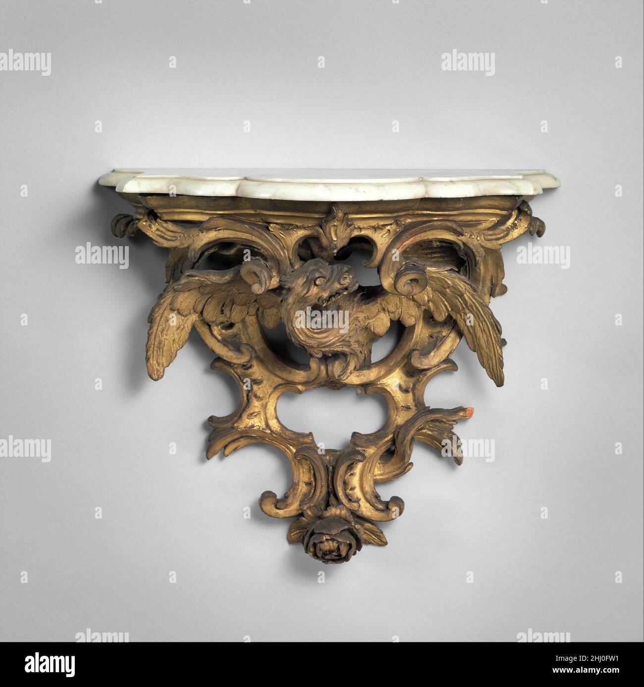 Wandhalterung (Konsolenapplikation) ca. 1715–20 Französische kleine Wandhalterungen (Consoles d’applique) mit Porzellanvasen, Uhren oder Kerzenleuchtern, die in der Regel mit der Inneneinrichtung eines Raumes harmonieren. Diese besondere Halterung ist aus Terrakotta gefertigt und kann ein Modell für einen Holzschnitzer oder eine Bronzerolle gewesen sein, die später vergoldet und zum Aufhängen montiert wurde. Unter der Oberseite ist ein Drache mit ausgestreckten Flügeln geschnitzt, dessen langer Schwanz um durchbrochenes C und umgekehrte C-Rollen verschlitzt ist. Diese Halterung war Teil der Modellsammlung für Holzarbeiten, Verkleidungen und Sitzmöbel von Maison Leys, A Stockfoto