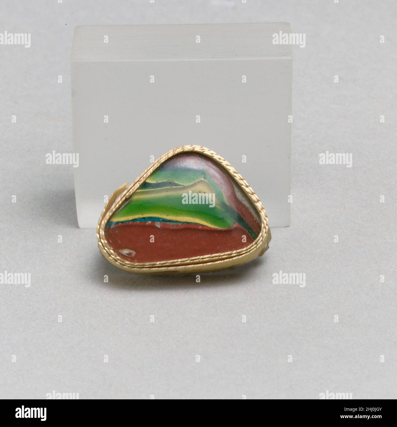 Glasmosaik-Schalenfragment Ende des 1st. Jahrhunderts v. Chr.–Anfang des 1st. Jahrhunderts n. Chr. Römisches Körperfragment.Durchscheinendes Türkisblau, mit opakes Gelb geschichtet und grün, opakes Gelb und Ziegelrot, farblos.konvex geschwungene Seite.geschichtete gewellte Bänder aus Rot, Grün und Gelb in einem unregelmäßigen Muster.Polierte Außenseite; Lochfraß und Verwitterung der Oberflächenblasen; Stumpfen, Lochfraß und schillernde Verwitterung auf dem Innenraum und an den Kanten. In ein Dreieck mit abgerundeten Ecken schneiden. Glasmosaik Schale Fragment 257306 Stockfoto